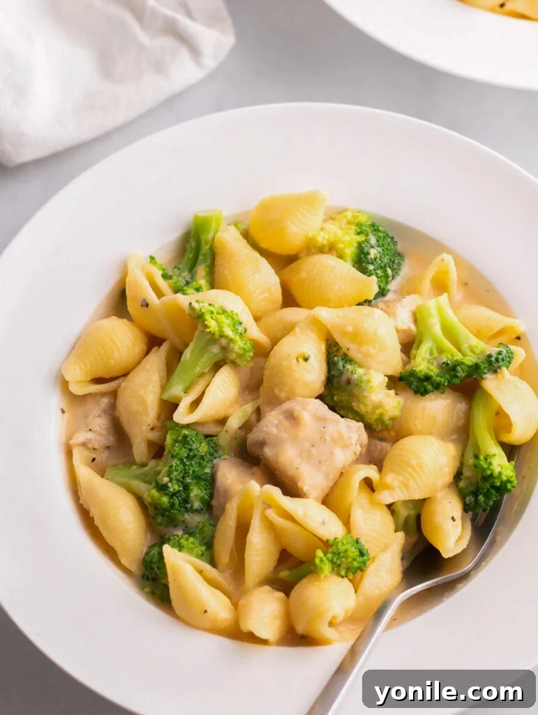 Creamy broccoli mac and cheese in a white plate with a fork, ready to be enjoyed.