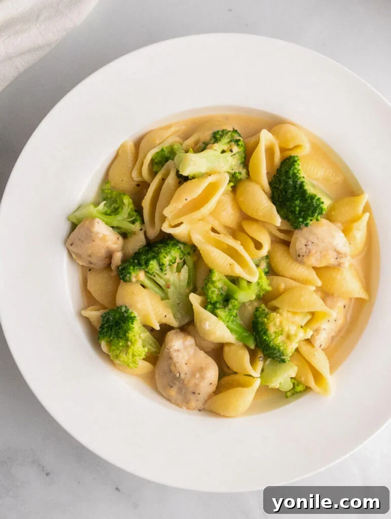 Creamy broccoli chicken mac and cheese served on a white plate with a side dish.