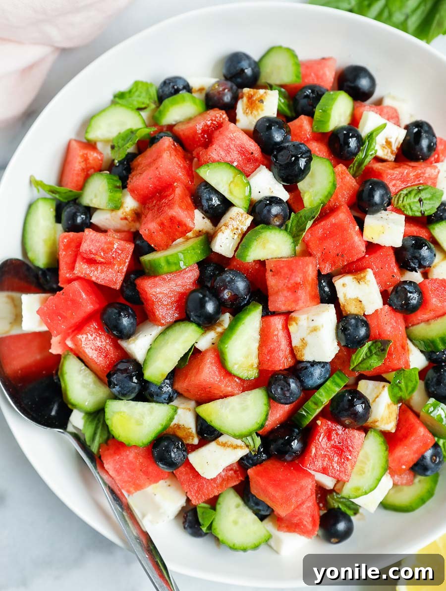 top down shot of the watermelon cucumber feta salad in a white bowl, garnished with basil