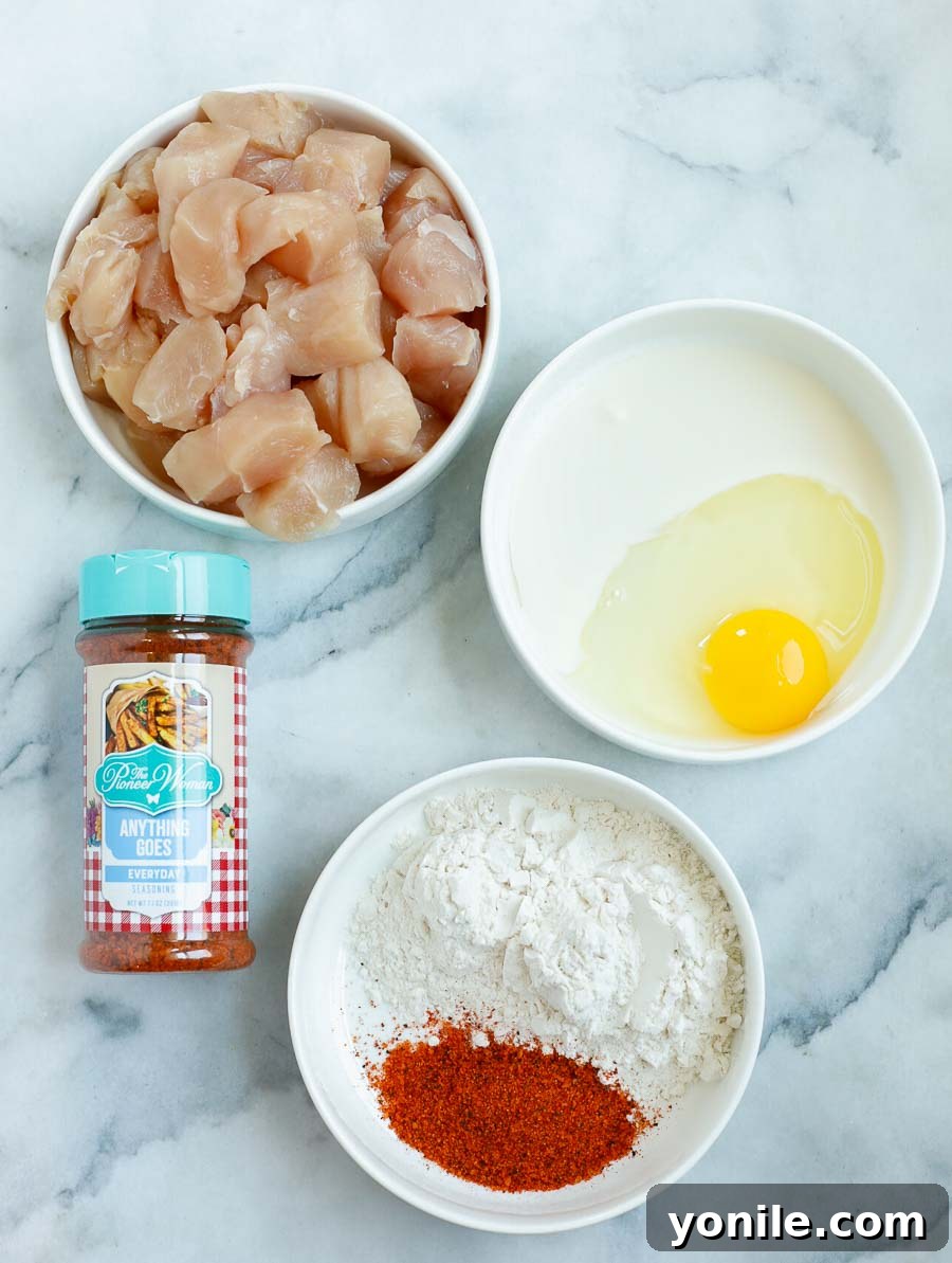 Addictive Chicken Crisps 3 Individual ingredients laid out for crispy chicken bites, including cubed chicken, flour, seasoning, egg, heavy cream, and canola oil.