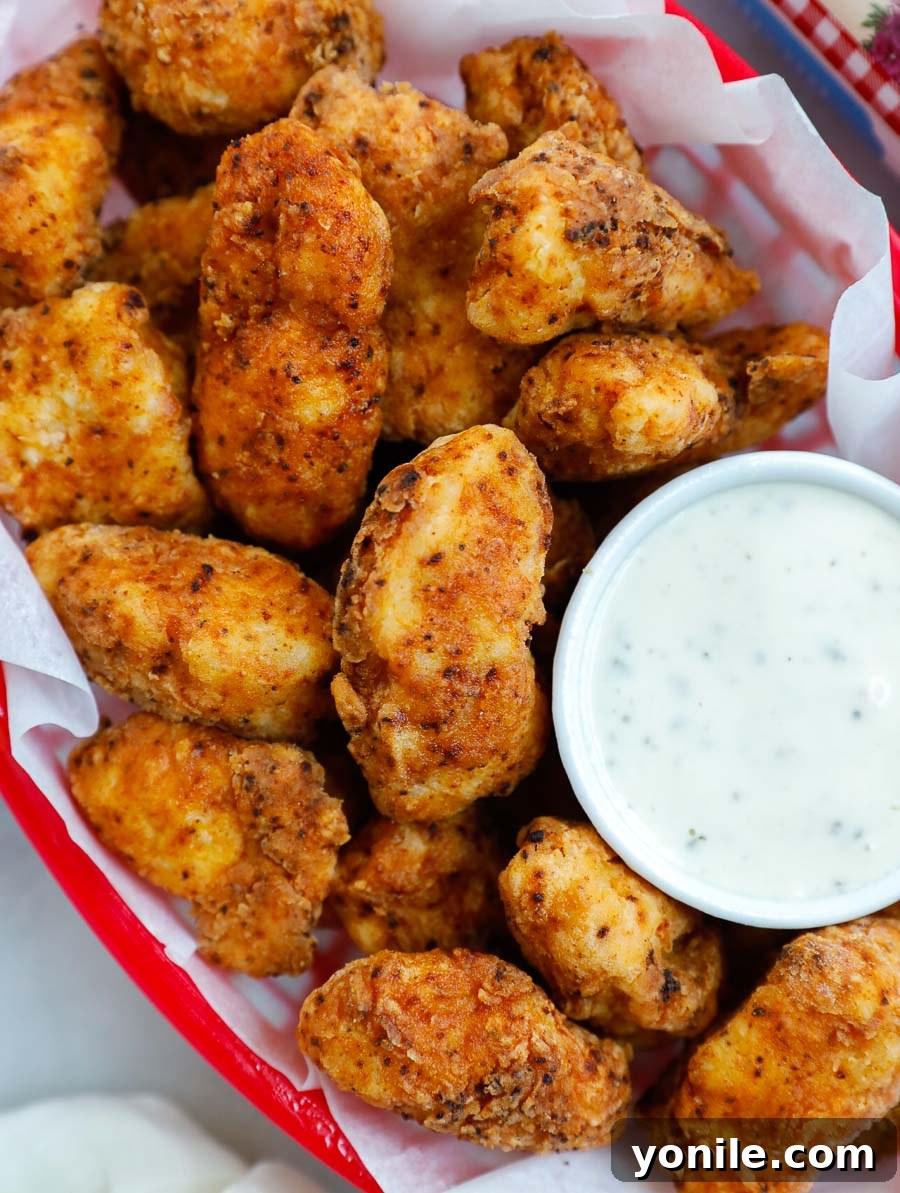 Addictive Chicken Crisps 7 A basket full of golden crispy chicken bites, accompanied by a side of ranch dipping sauce, ready to be enjoyed.