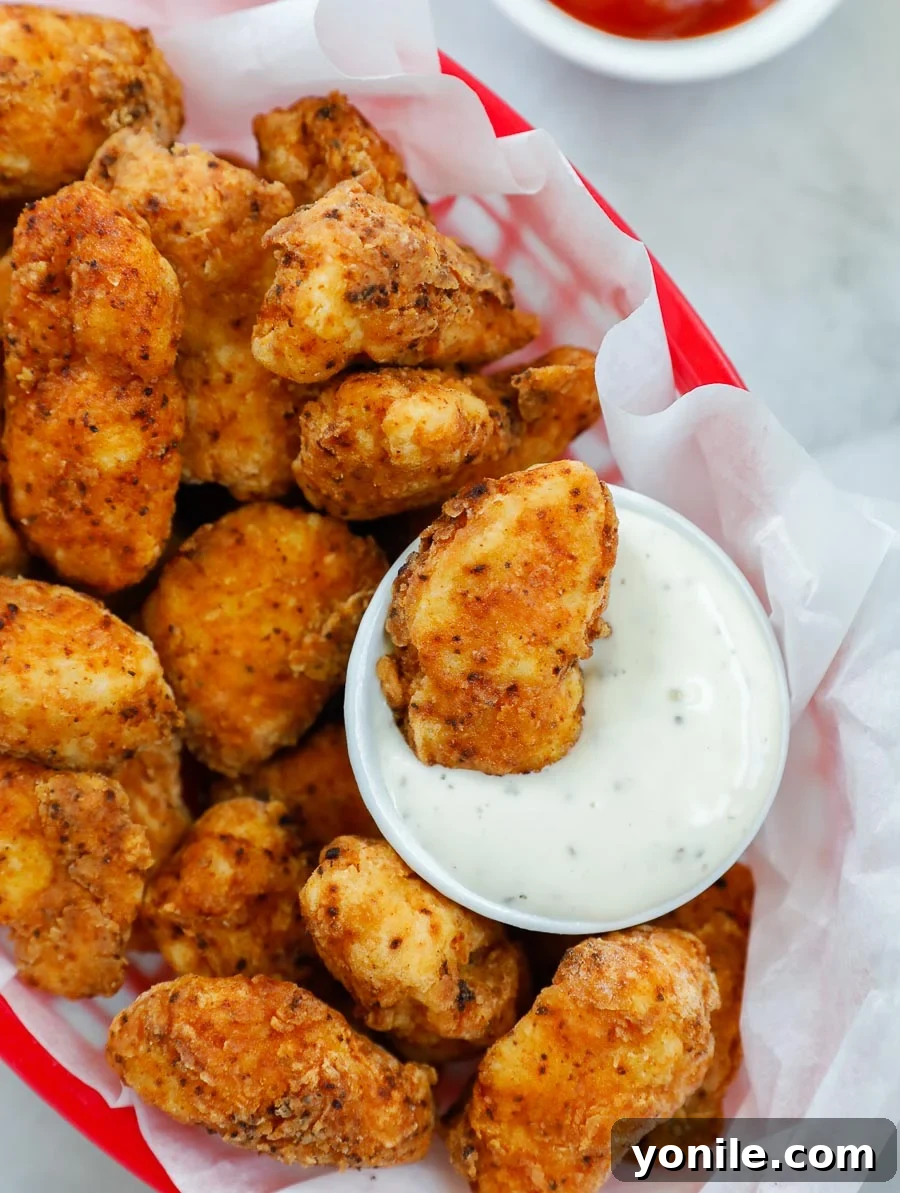 Addictive Chicken Crisps 8 A vibrant close-up of crispy chicken bites in a red basket, with one piece dipped in ranch sauce, showcasing its appealing texture.