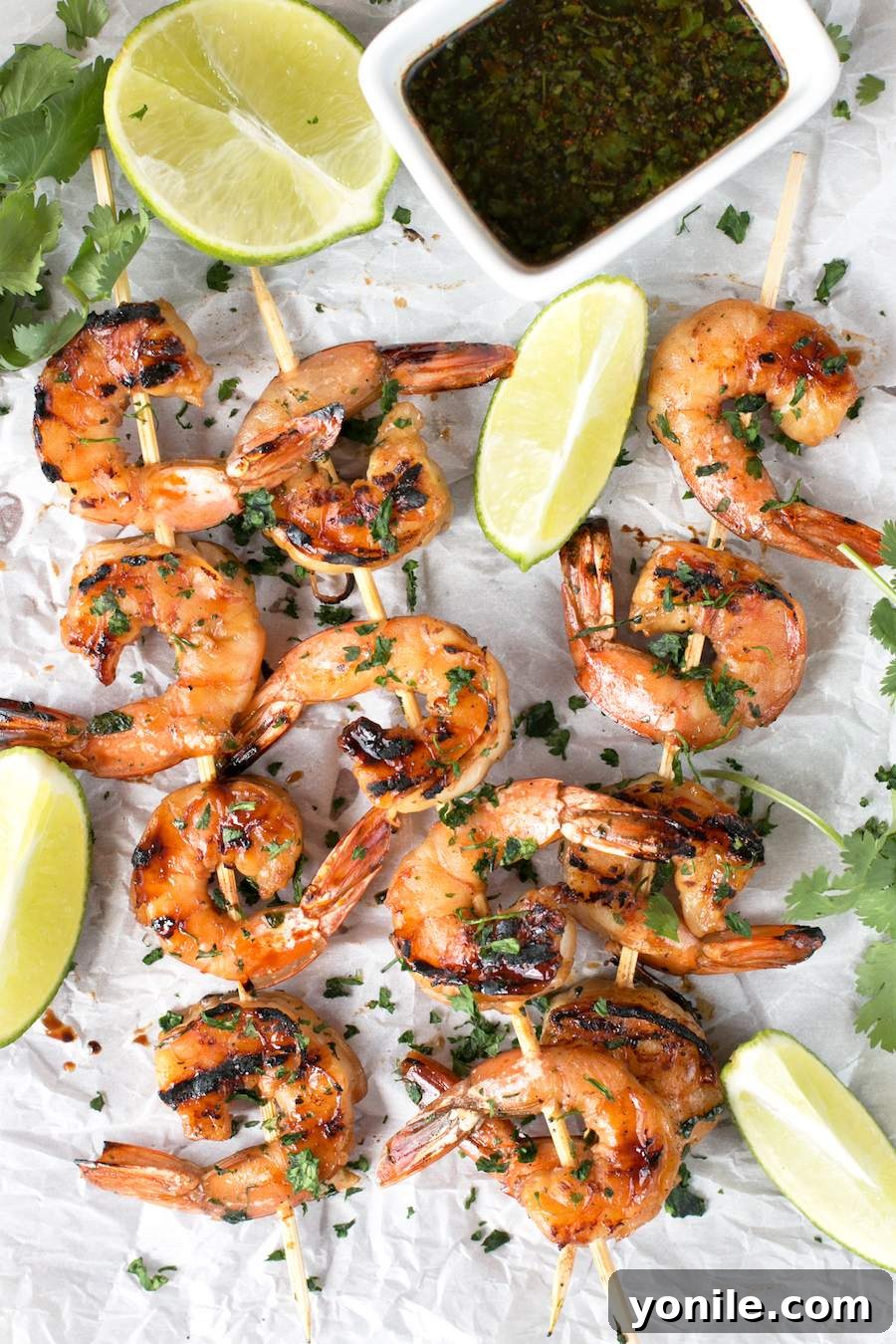 Agave Cilantro Shrimp Skewers with dipping sauce and lime on parchment paper. Agave Cilantro Shrimp Skewers with dipping sauce and lime on parchment paper.