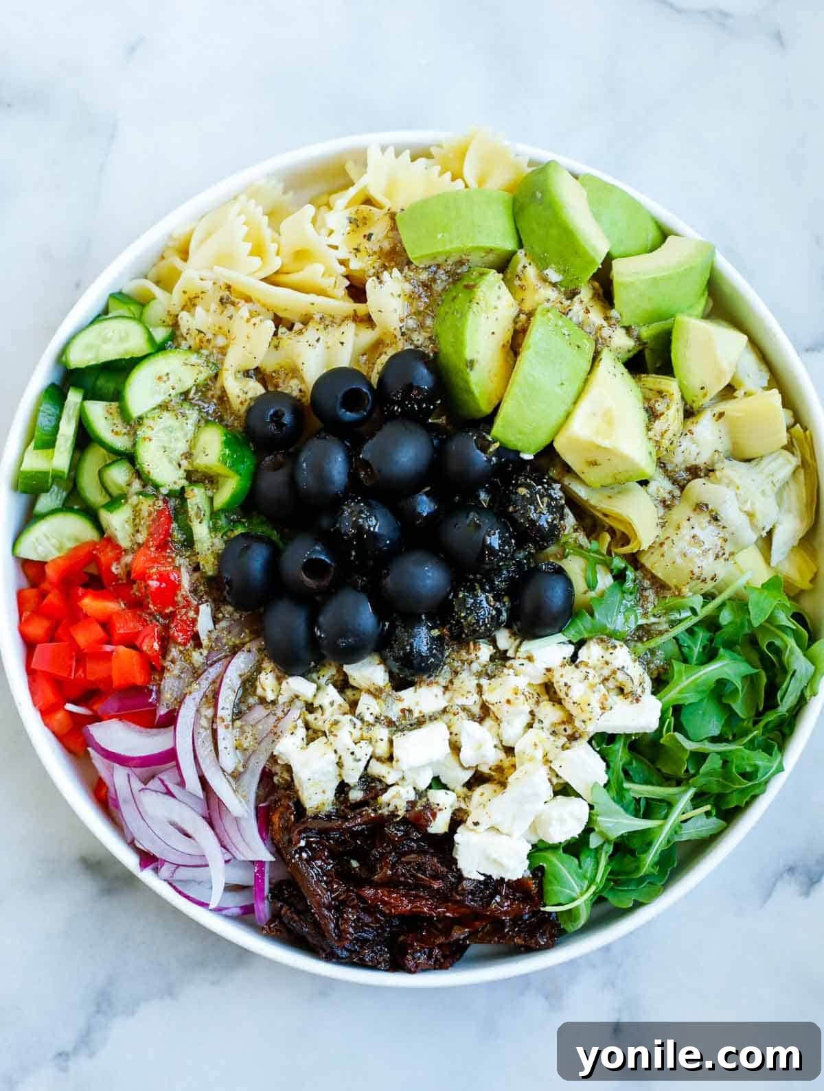 Zesty Mediterranean Pasta Salad 7 Salad dressing added to a bowl of Mediterranean salad.