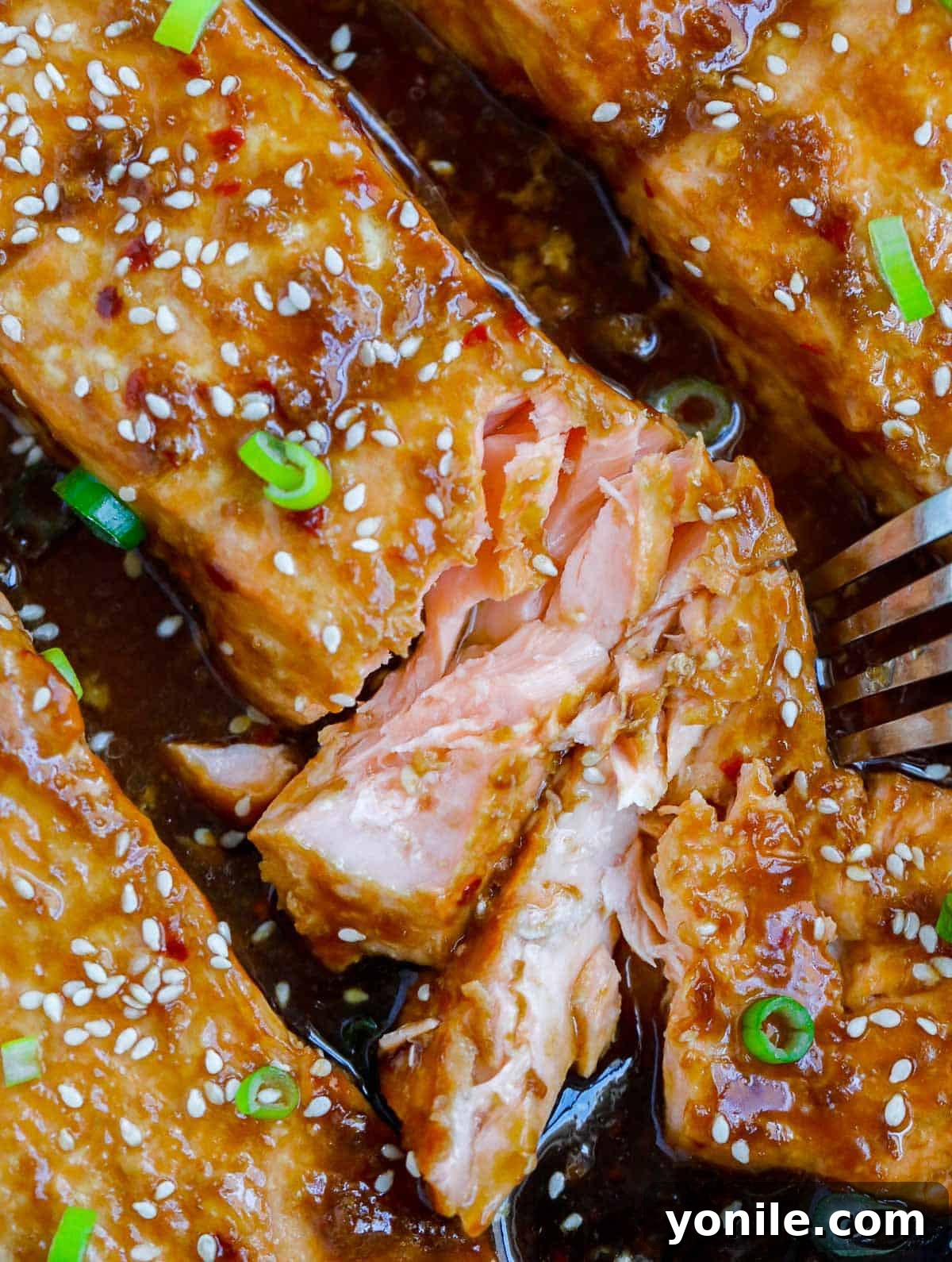 Golden Teriyaki Salmon Bake 7 A fork flaking a piece of perfectly cooked teriyaki salmon, demonstrating its tender and moist texture.