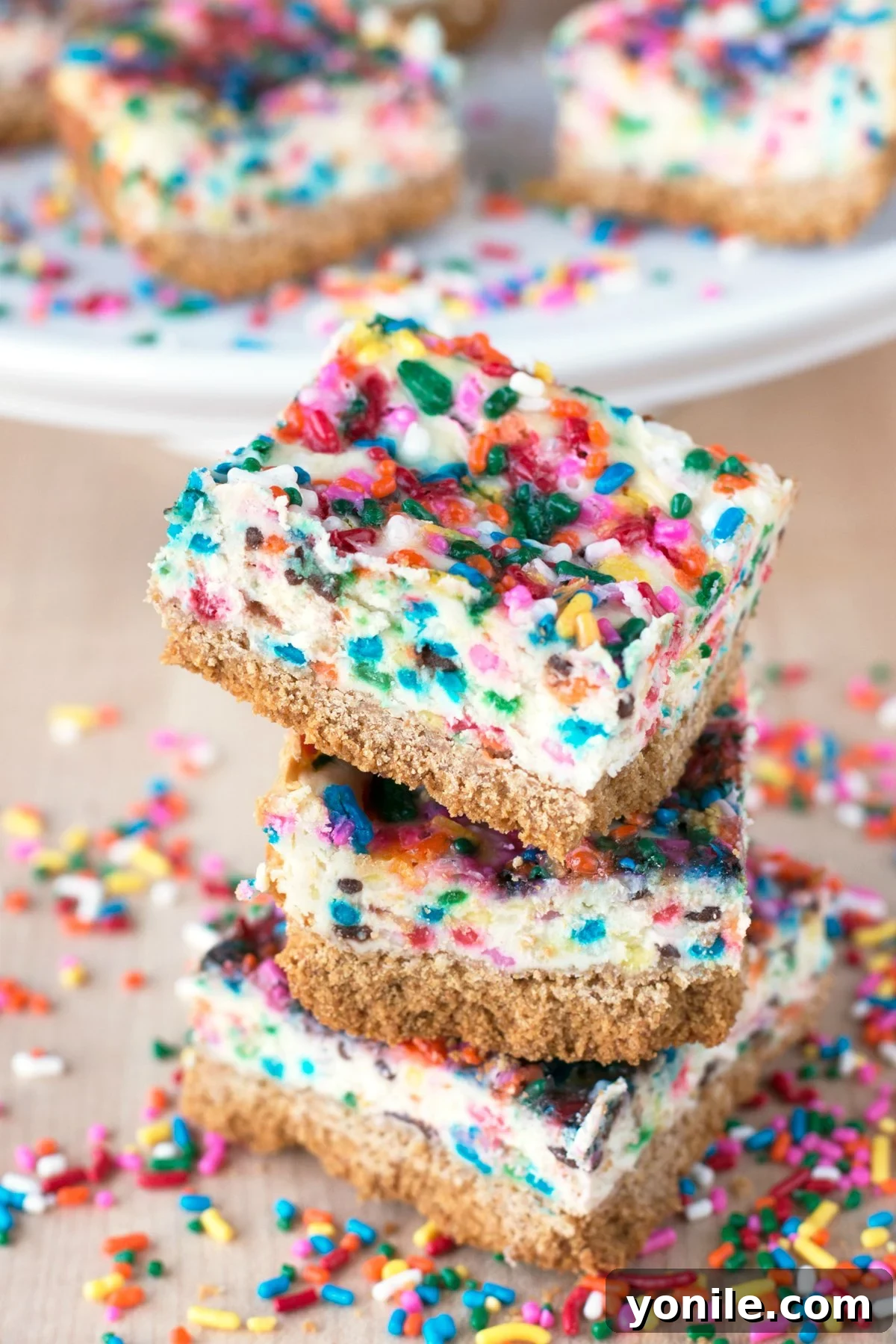Three funfetti cheesecake bars stacked on a table and surrounded by spirnkles