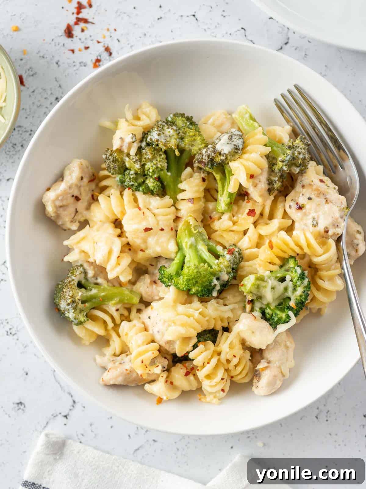 Homestyle Baked Chicken and Broccoli Pasta 11 A fork resting on the side of a plate filled with baked chicken and broccoli pasta, ready to be enjoyed.