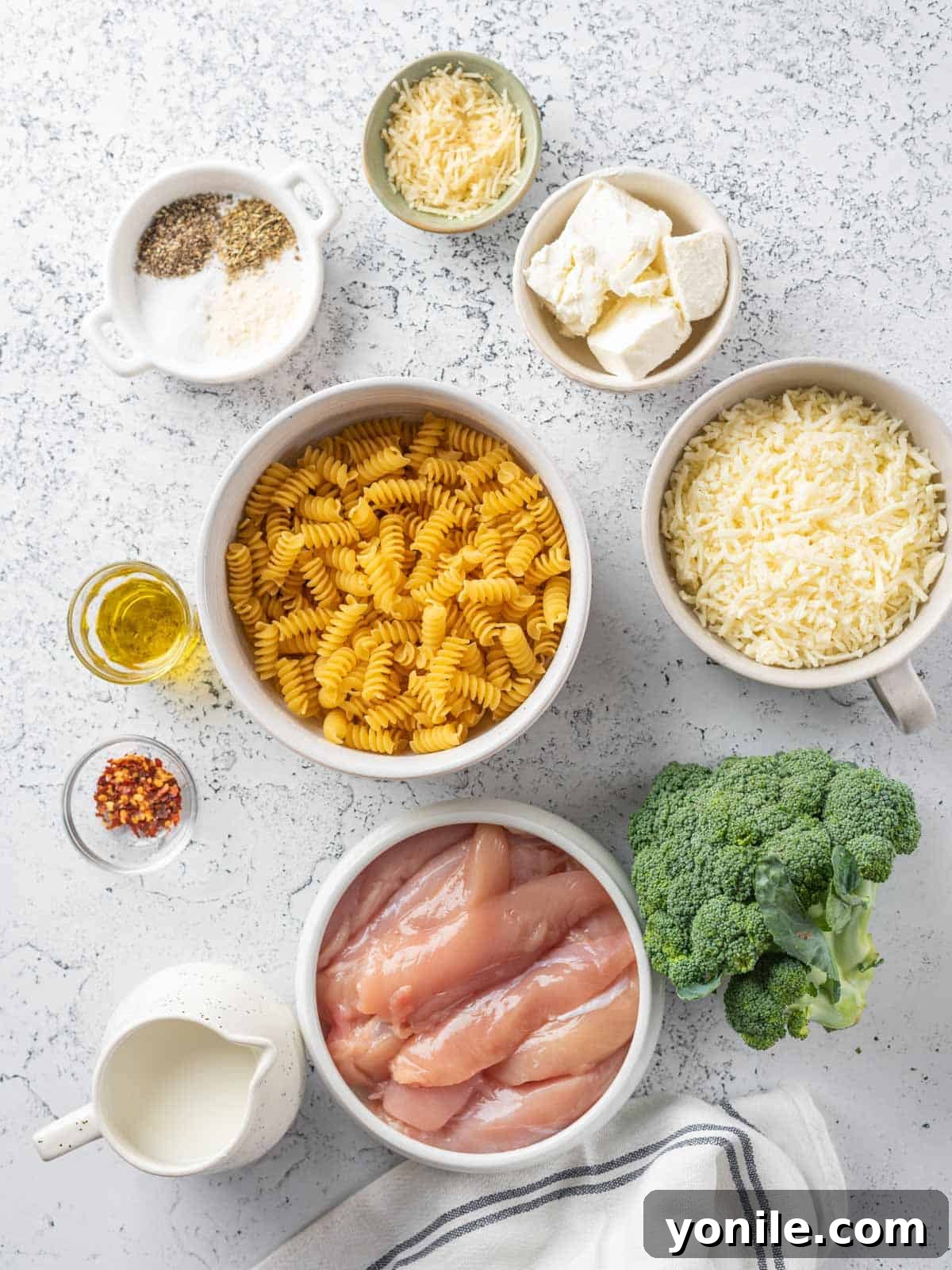 Homestyle Baked Chicken and Broccoli Pasta 3 A collection of fresh ingredients laid out, including uncooked pasta, fresh broccoli florets, chicken pieces, various seasonings, and dairy products like cream cheese and mozzarella, ready for the baked chicken and broccoli bake.