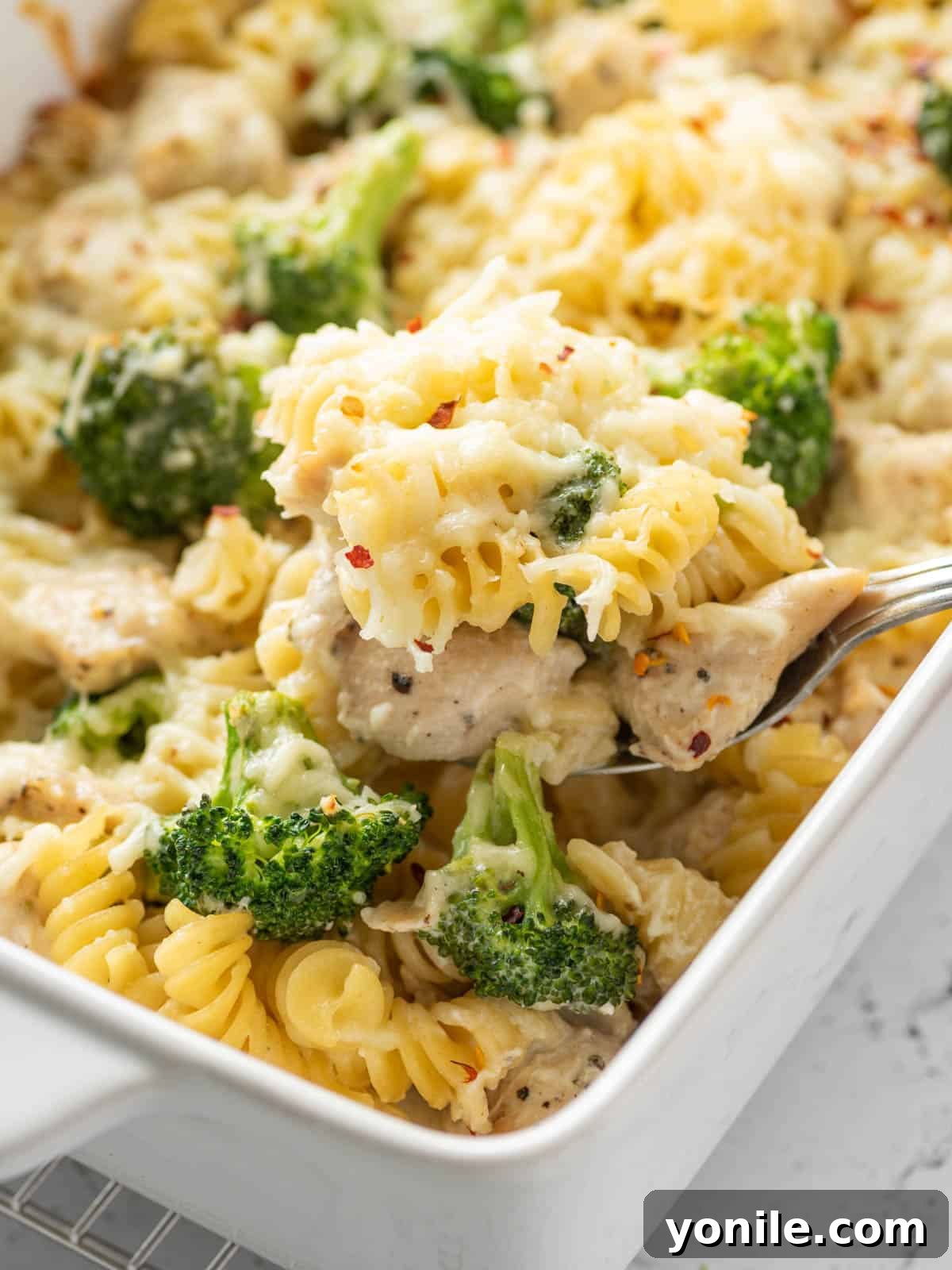 Homestyle Baked Chicken and Broccoli Pasta 10 A spoon scooping a generous portion of the creamy baked chicken, broccoli, and pasta bake onto a plate, highlighting the delicious texture and ingredients.