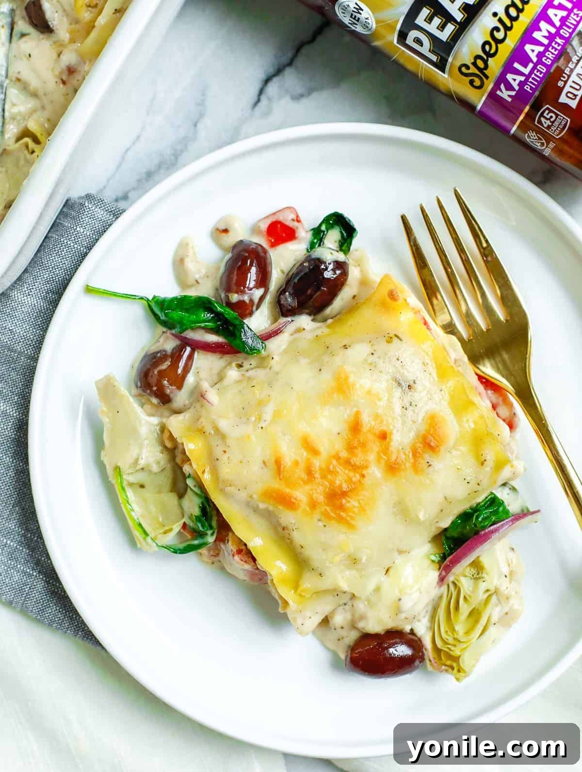 Piece of Greek White Alfredo Lasagna Roll on a plate with a gold fork