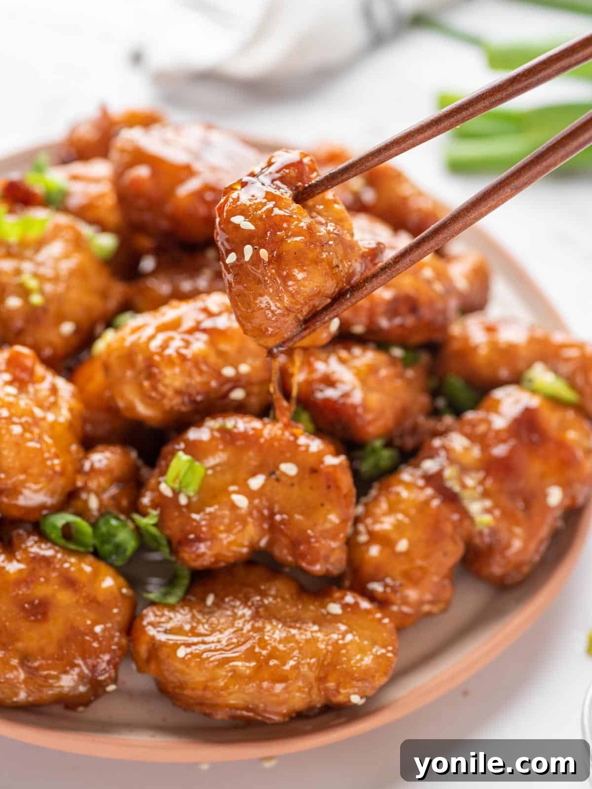 A plate with Crispy Honey Chicken with a pair of chopsticks lifting a piece up, showcasing the golden crispness and glossy sauce.