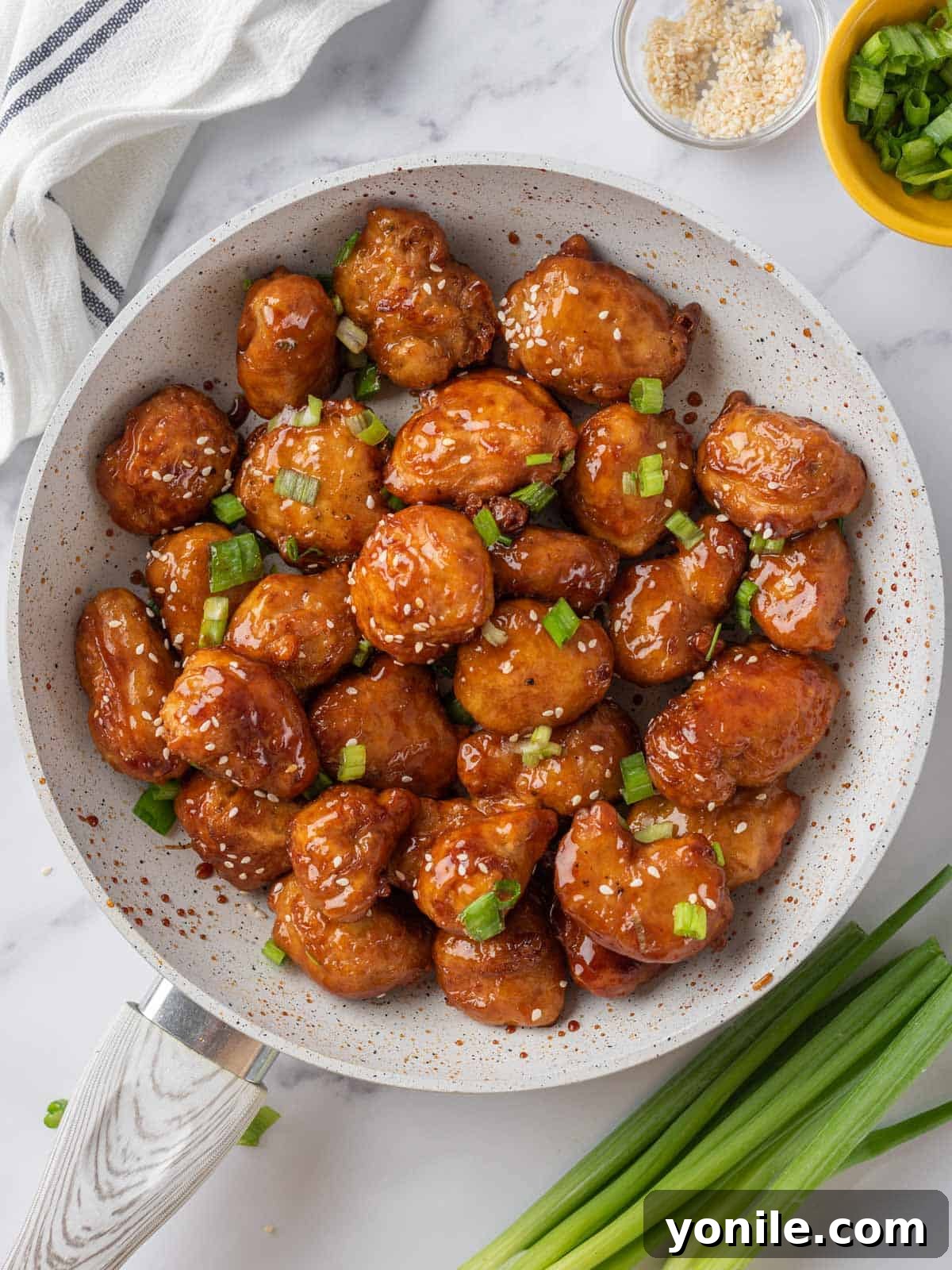 A pan full of freshly made Crispy Honey Chicken, coated in sauce and garnished, ready to serve.