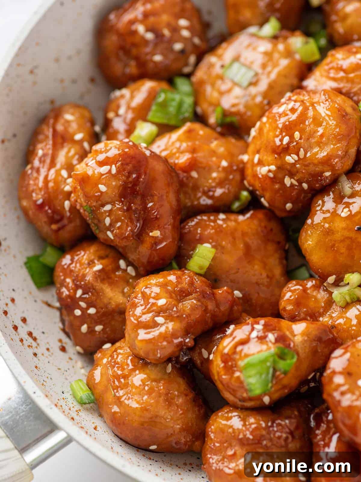 Close up shot showing glistening pieces of crispy honey chicken in a pan, highlighting the sauce and texture.