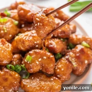 A plate with Crispy Honey Chicken with a pair of chopsticks lifting a piece up.