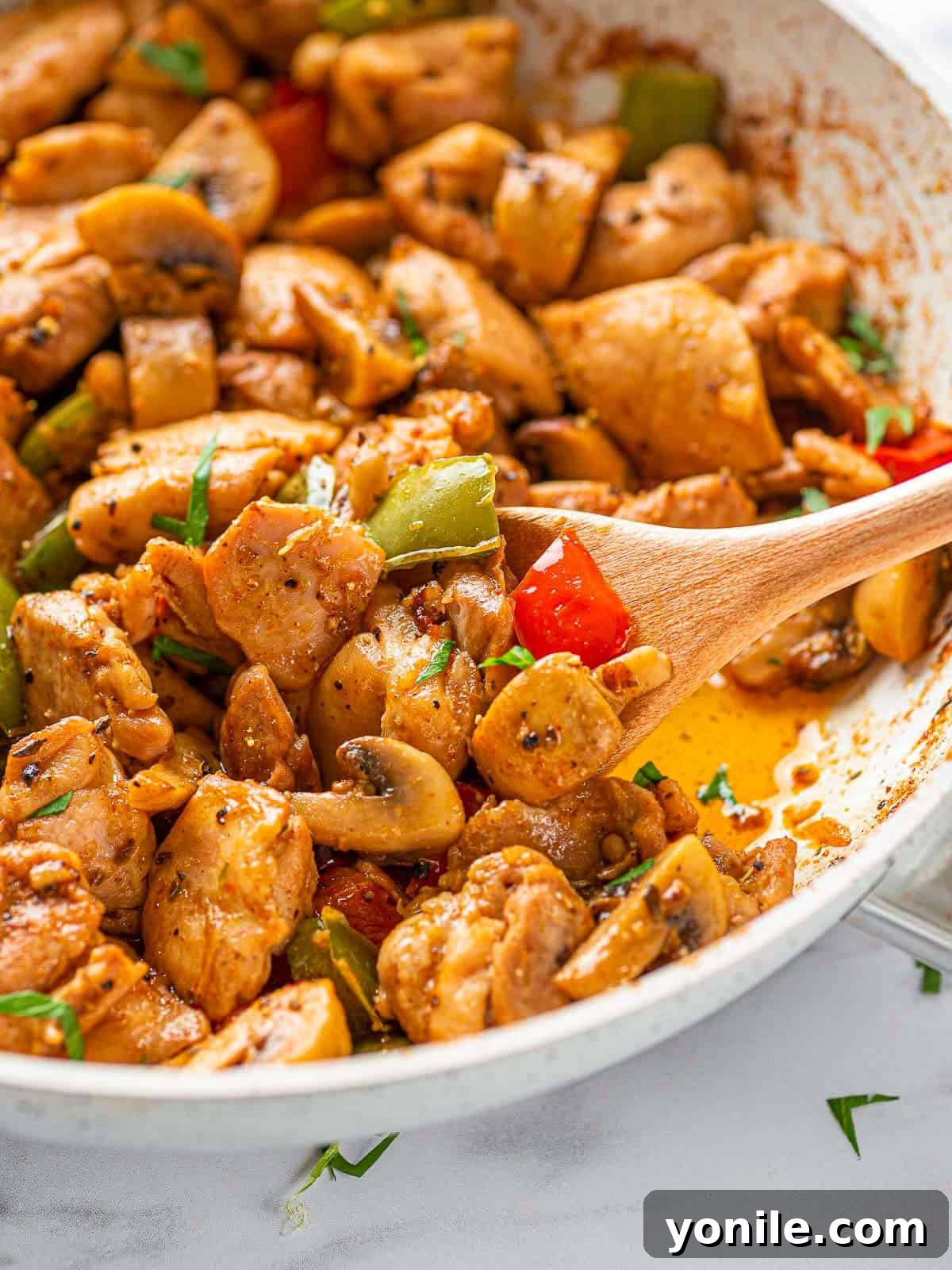 Sizzling Garlic Butter Mushroom Chicken Bites 7 A pan full of finished Garlic Mushroom Chicken Bites, garnished with fresh parsley, with a wooden spoon ready to serve.