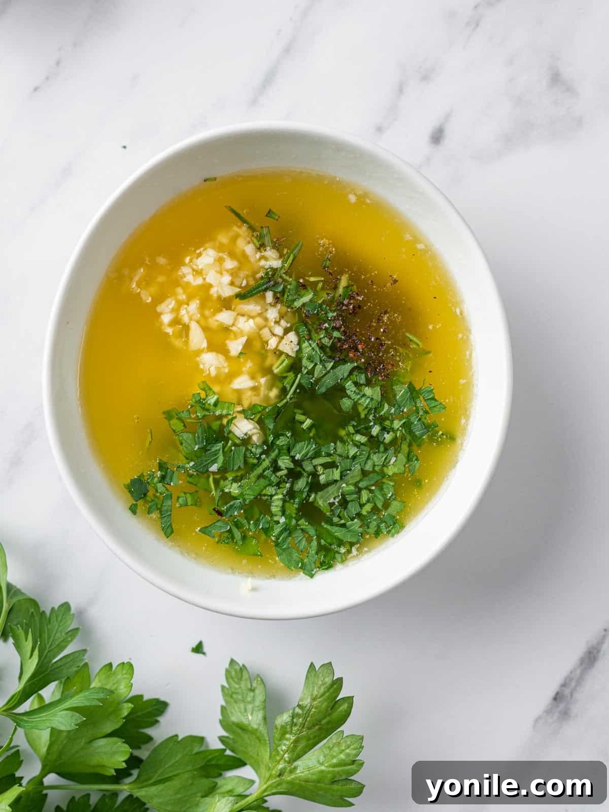 Melted butter infused with fresh herbs and minced garlic in a bowl, ready to be applied to the chicken.