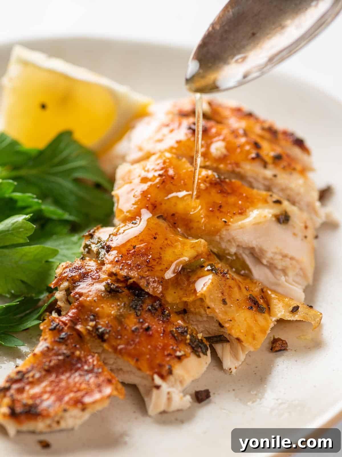 Close-up of perfectly sliced chicken breast, with glistening juices drizzled over top, highlighting its tenderness.