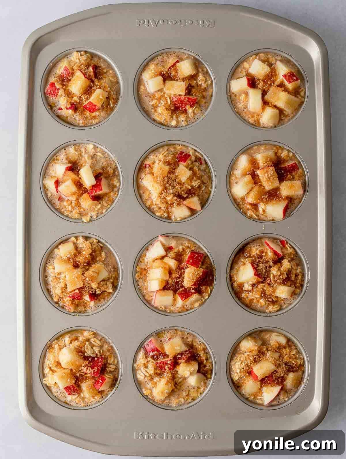 Overhead view of cinnamon baked apple oats cups in a muffin tin, ready for the oven.