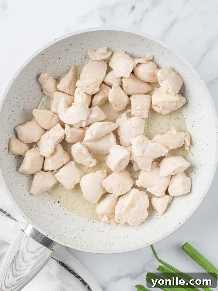 Sautéed cubed chicken pieces sizzling in a hot skillet, achieving a golden-brown sear.