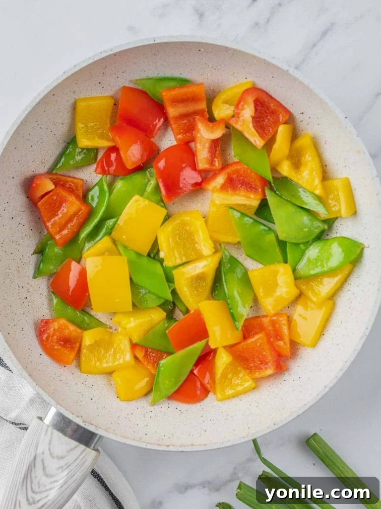 Vibrant red and yellow bell peppers along with crisp snow peas beginning to stir-fry in a pan.