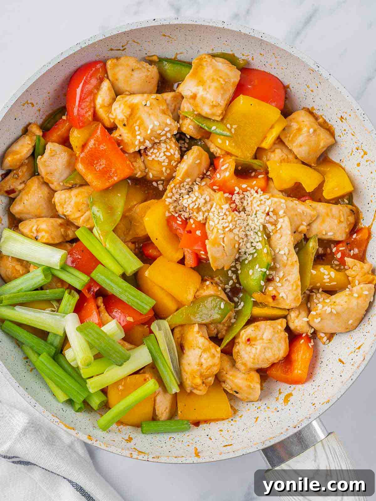 Sesame seeds and chopped green onions being added to the finished Szechuan chicken stir-fry in the pan.