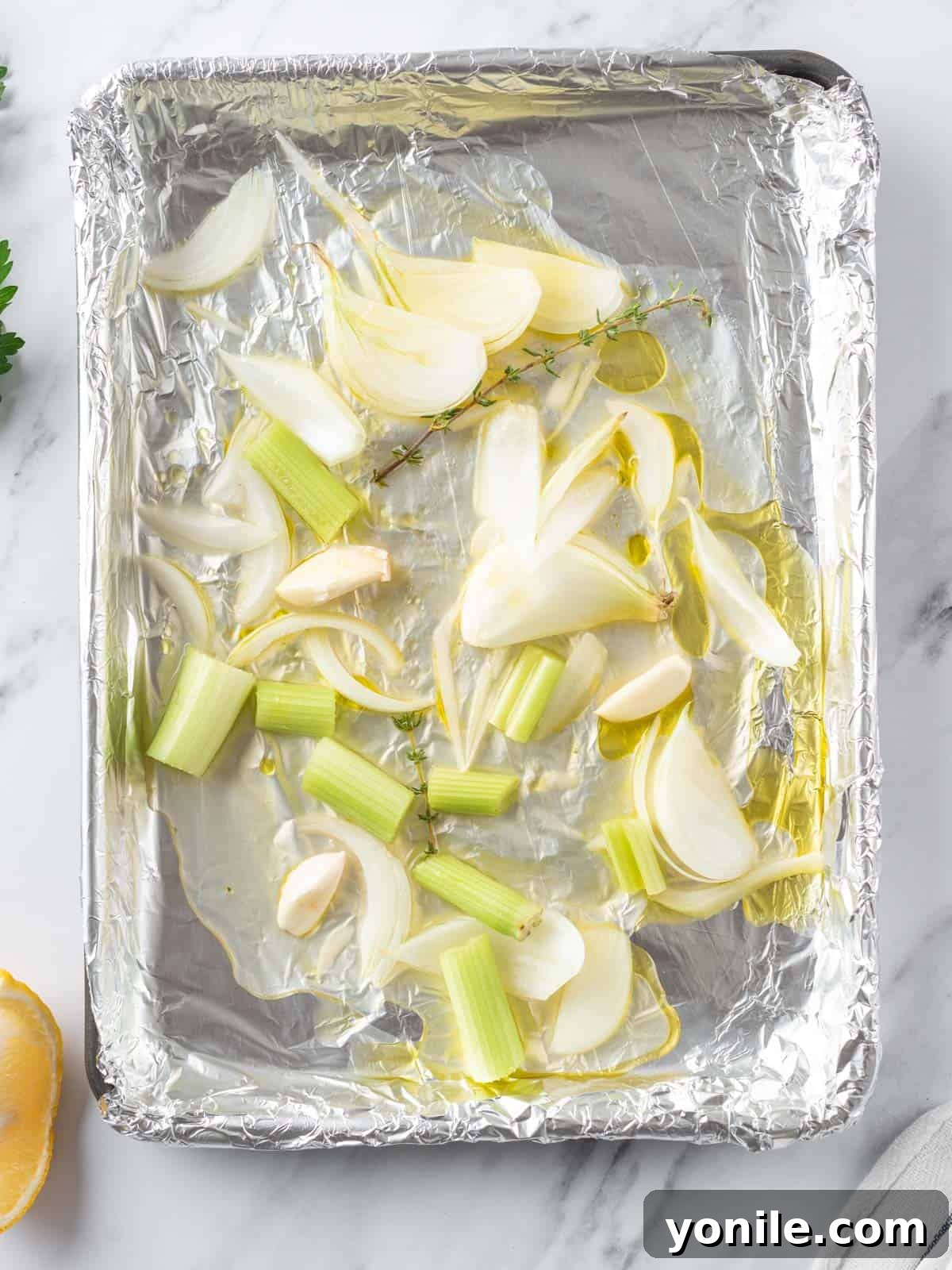 Succulent Spatchcock Roast Chicken 9 A roasting pan filled with chopped onions, celery, fresh thyme, and chicken broth, forming an aromatic base.