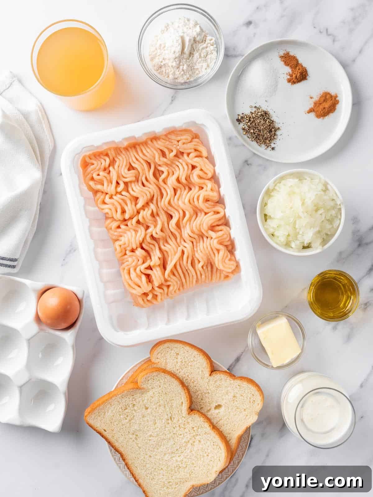 A selection of fresh ingredients laid out, including ground chicken, bread, onion, spices, butter, and cream, all essential for making Swedish meatballs.
