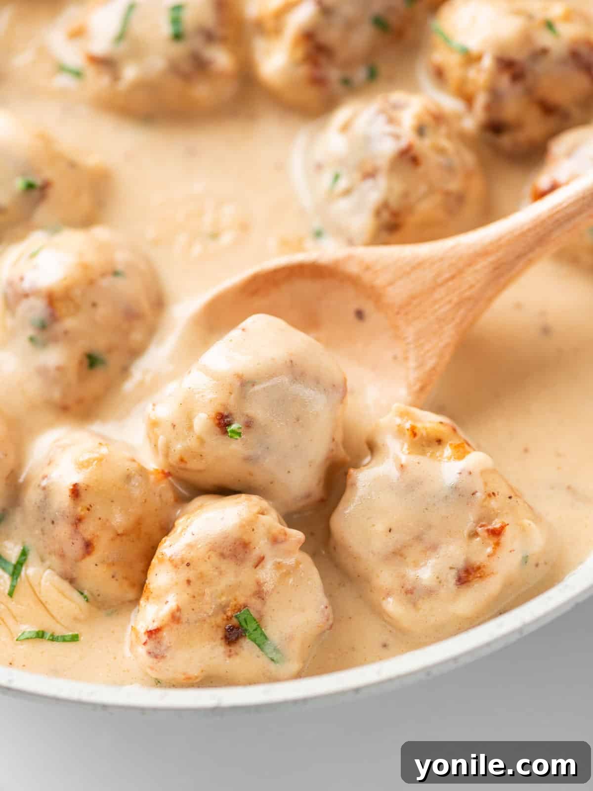 A close-up of a spoon scooping a chicken Swedish meatball from a plate, highlighting the creamy sauce and tender texture.