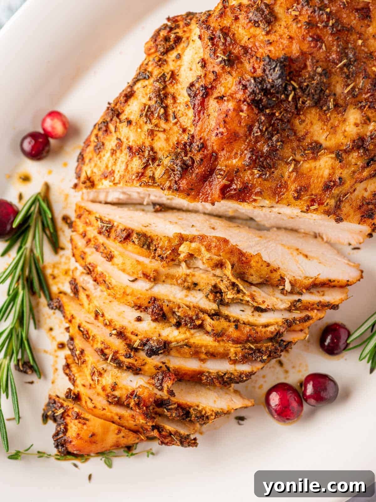 Perfectly Roasted Boneless Turkey Breast 7 overhead shot of a roasted turkey breast, expertly sliced halfway on a pristine white plate, adorned with festive cranberries and aromatic rosemary sprigs