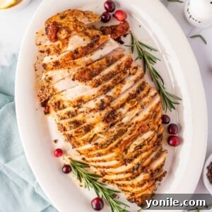 overhead shot of sliced turkey breast on a white plate with cranberry and rosemary stalks