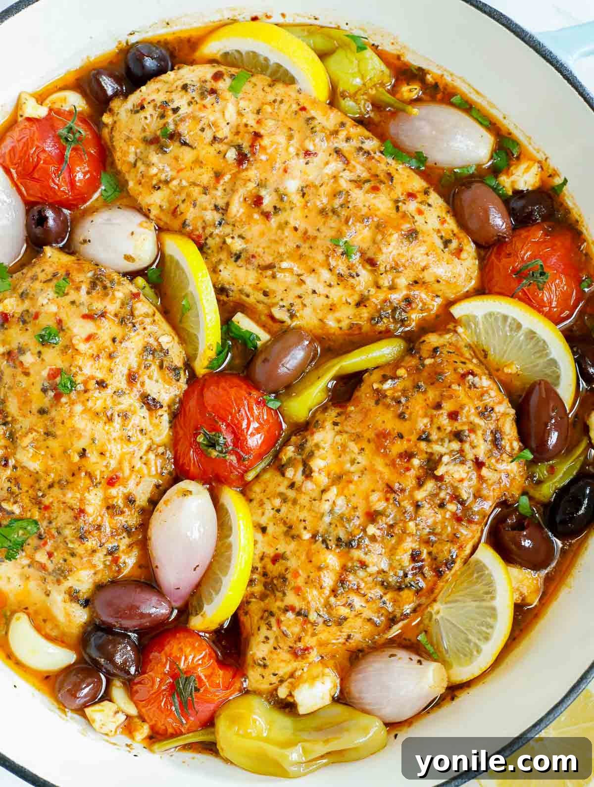 Overhead view of a pan of Greek chicken with fresh herbs and lemons.