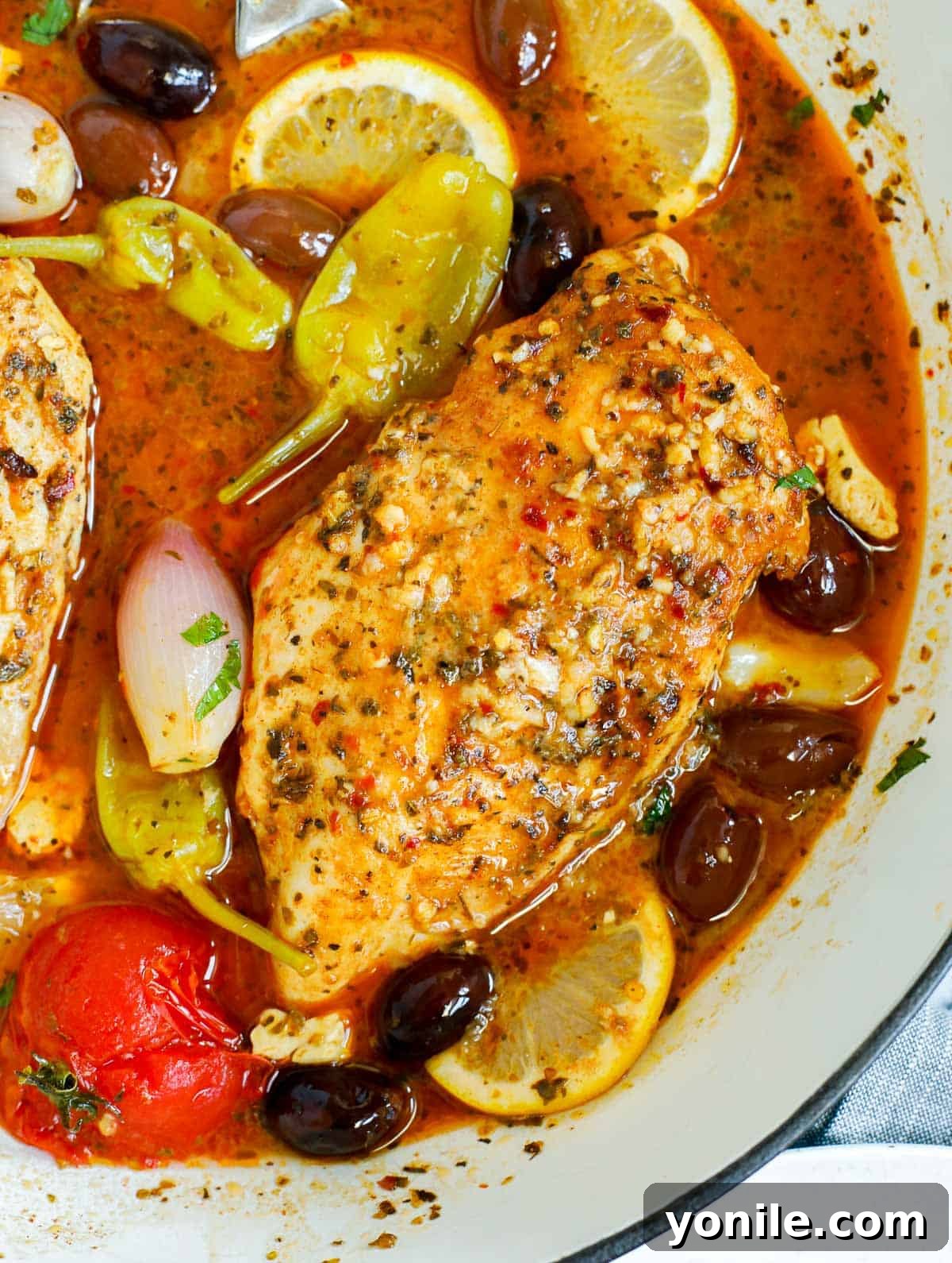 Close-up of a pan of oven baked Greek chicken breasts, garnished with fresh herbs.