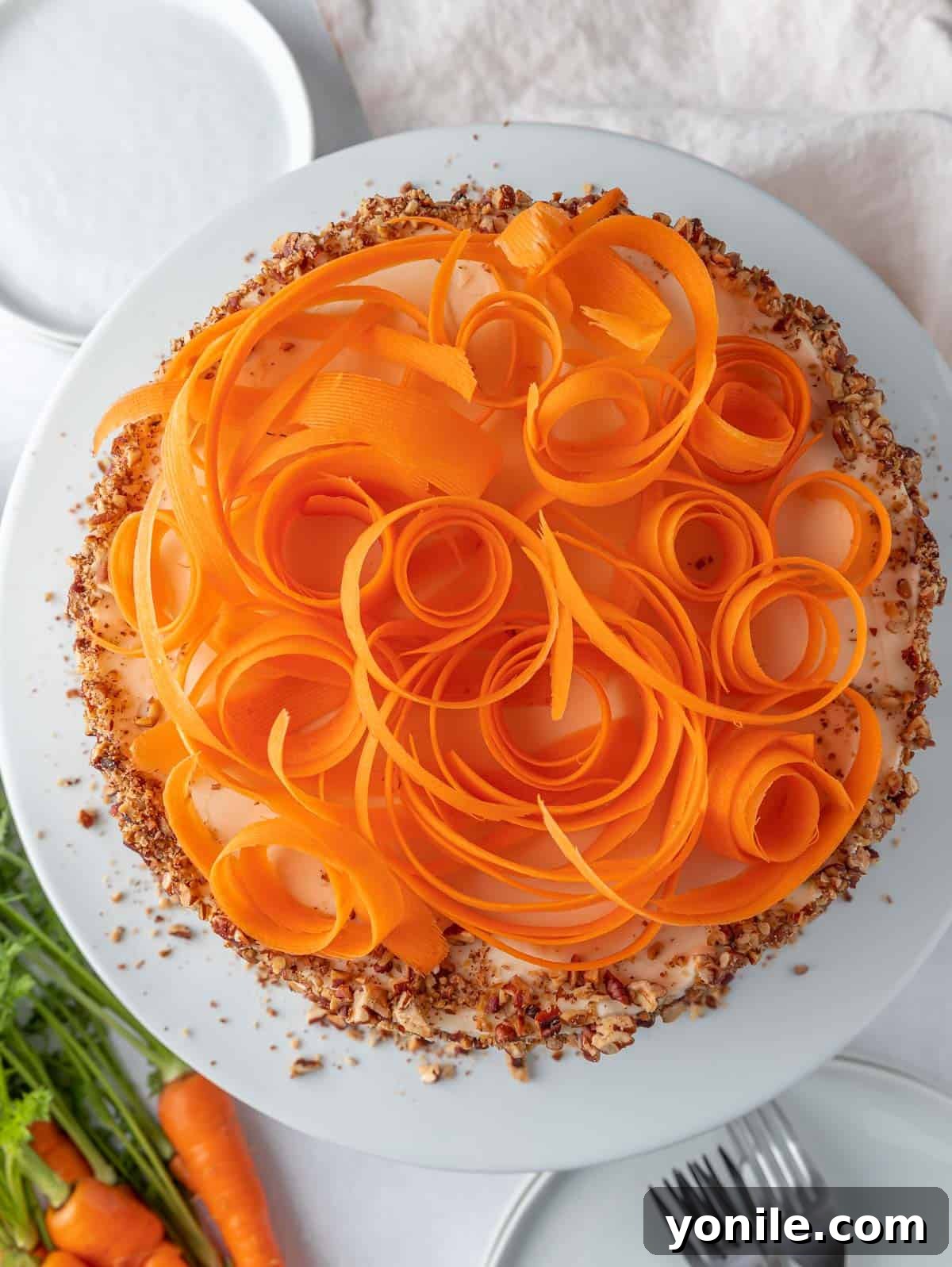 A whole, beautifully decorated carrot cake, topped with carrot shavings and nuts, displayed on a cake stand.