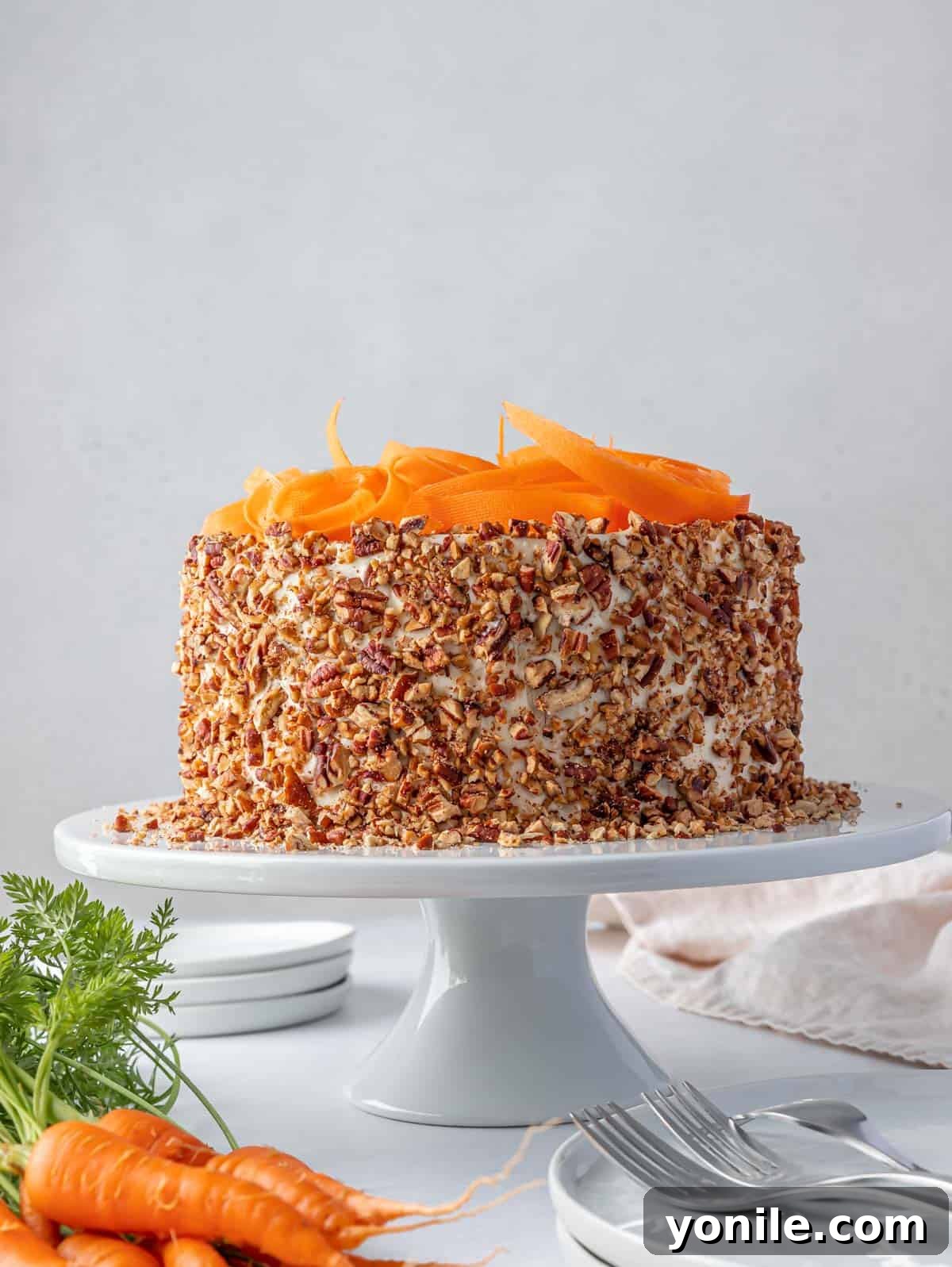 A whole, fully decorated carrot cake, adorned with pecans and carrot shavings, showcased on a elegant cake stand.