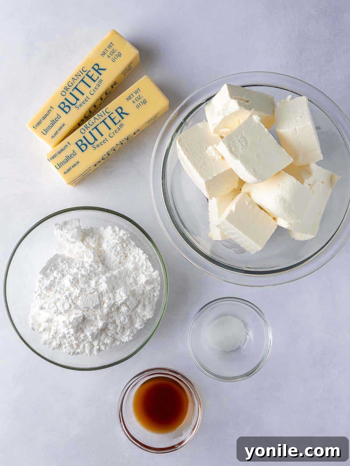 Individual ingredients for cream cheese frosting, including cream cheese bricks, butter sticks, powdered sugar, and vanilla extract.