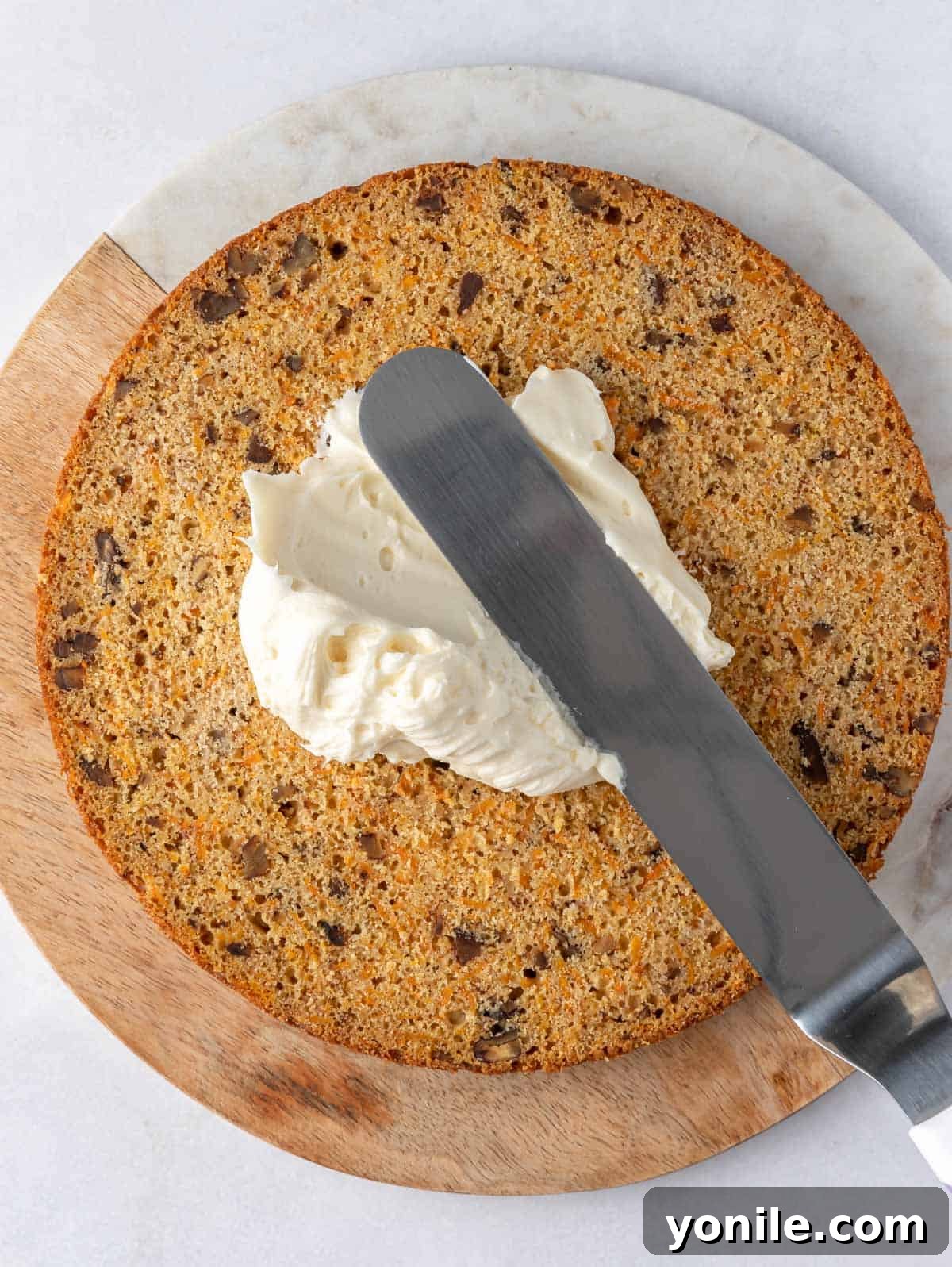 Close-up of a carrot cake being assembled, with cream cheese frosting spread between multiple cake layers.