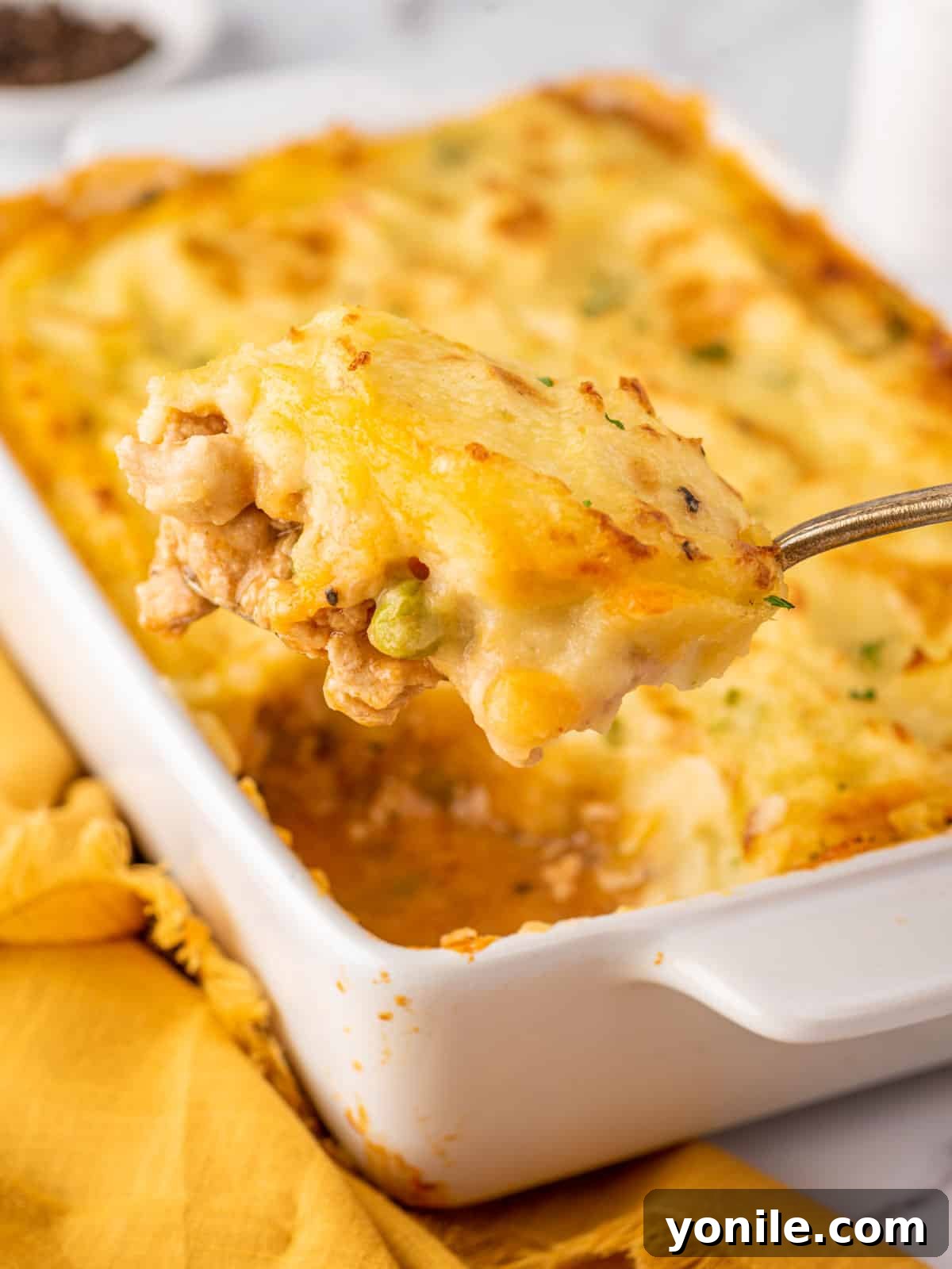 A serving spoon lifting a generous portion of Chicken Shepherd's Pie from the baking dish, showing layers of chicken and mashed potato