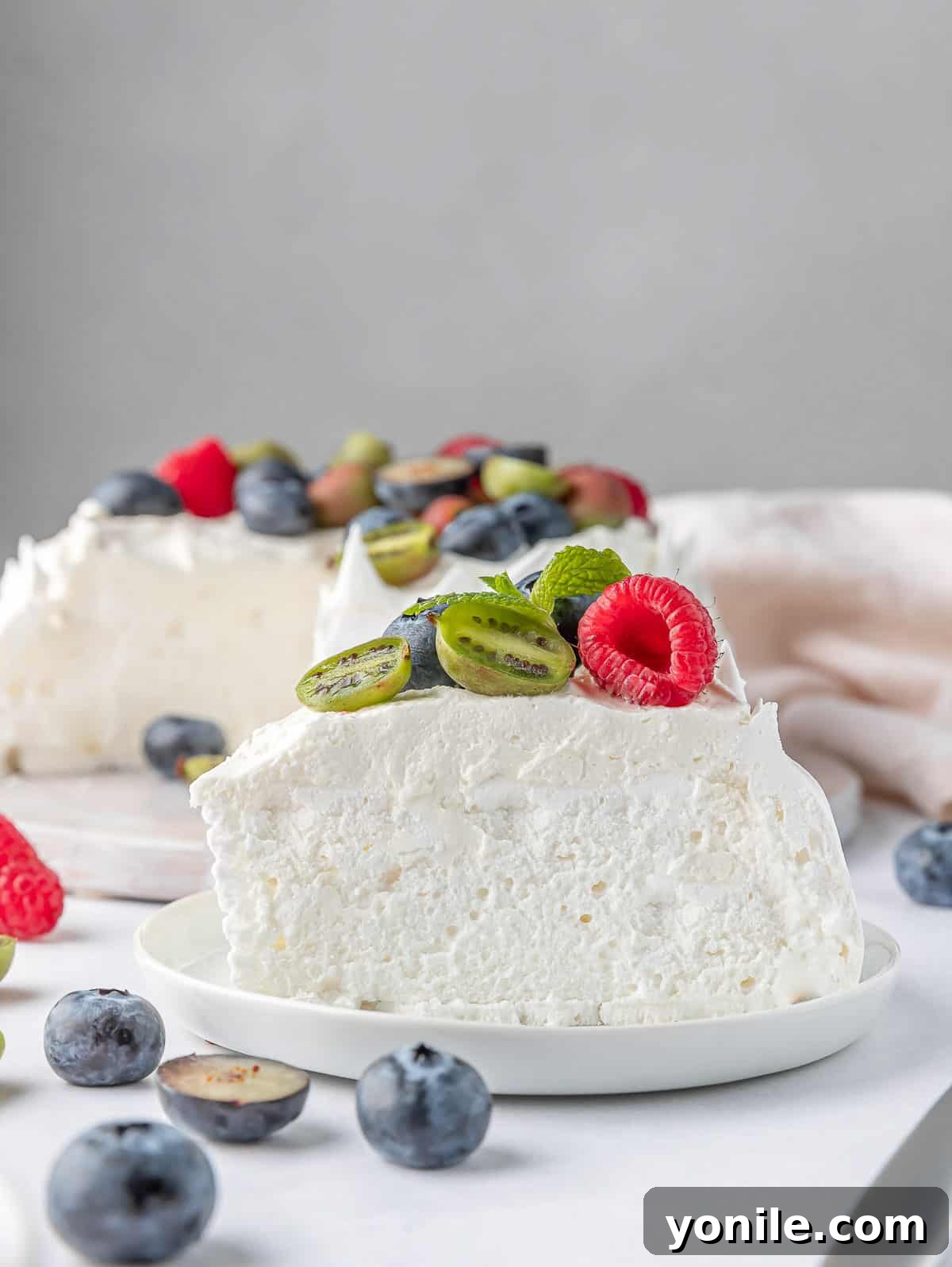 A beautifully plated slice of Berry Pavlova Cake on a white plate, showcasing its crispy meringue, creamy topping, and fresh berries.