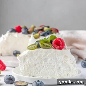 A beautifully plated slice of Berry Pavlova Cake on a white plate, showcasing its crispy meringue, creamy topping, and fresh berries.