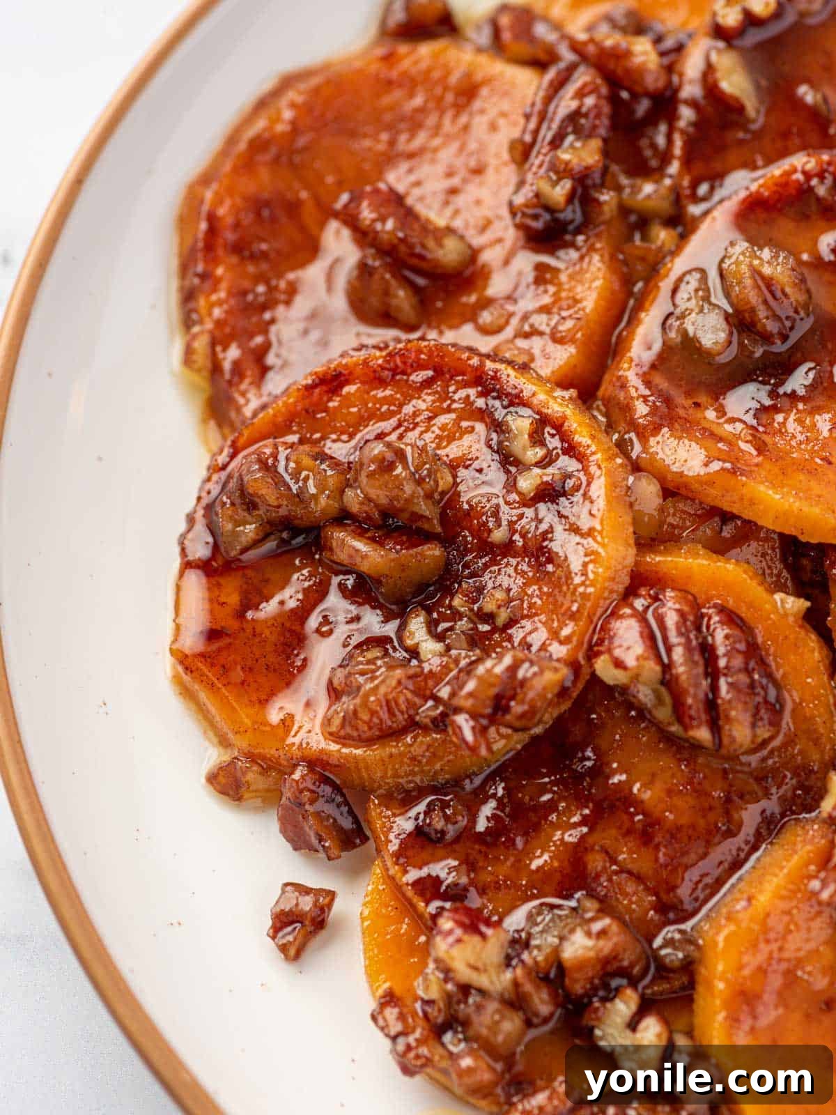 Close-up of a serving of candied sweet potatoes, highlighting the caramelized glaze and pecan pieces