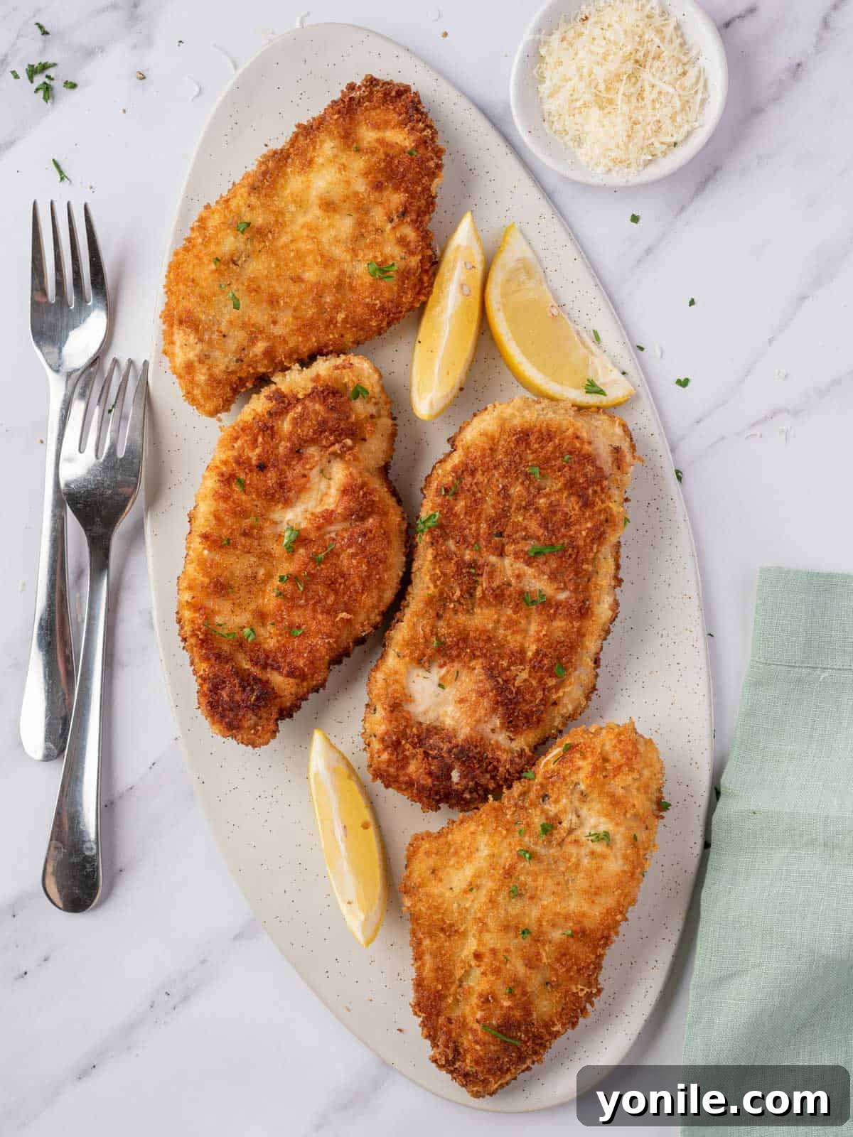 A platter of four crispy parmesan crusted chicken breasts, golden brown and garnished with fresh parsley.