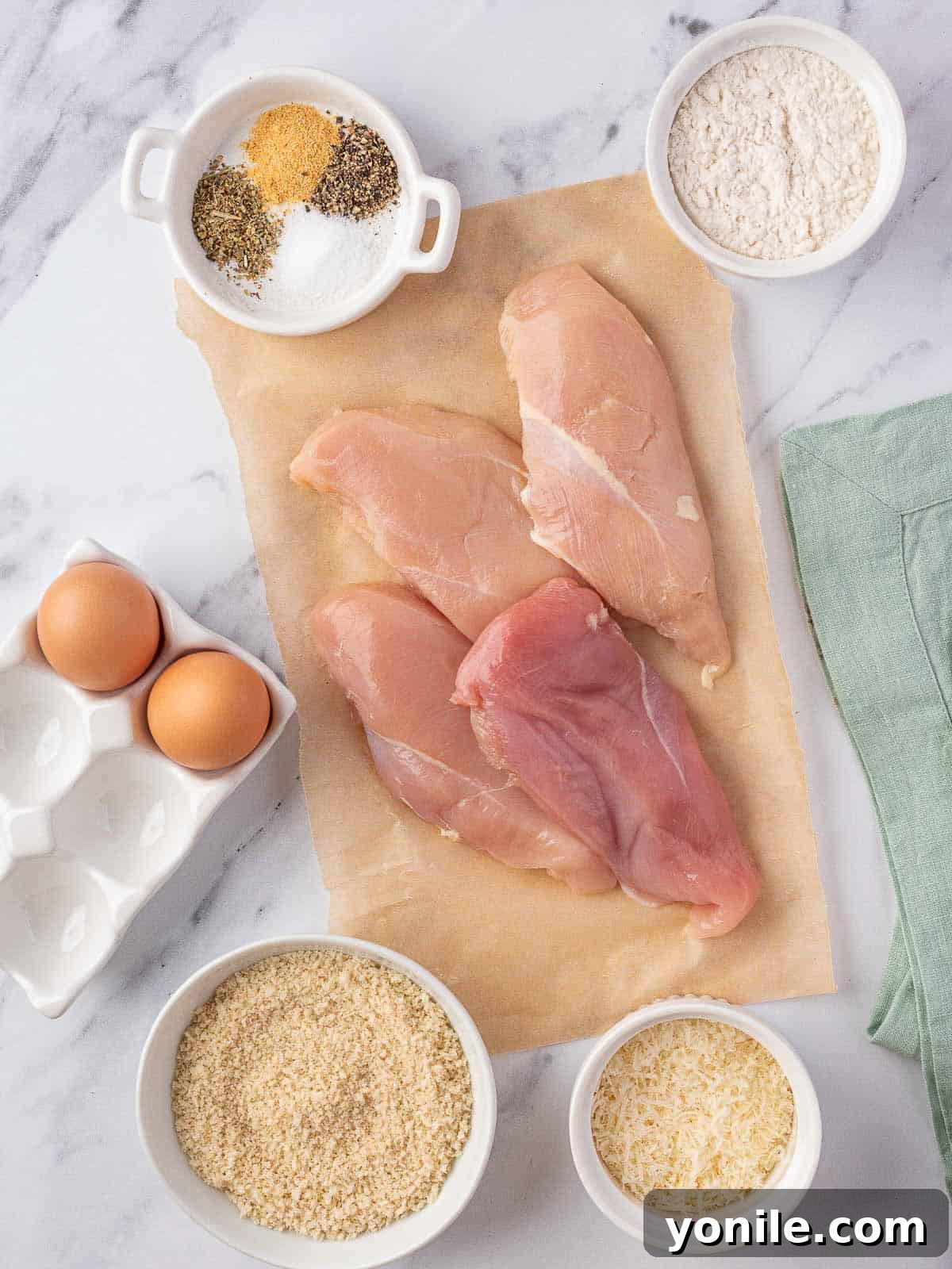 A collection of ingredients laid out on a table for making parmesan crusted chicken.