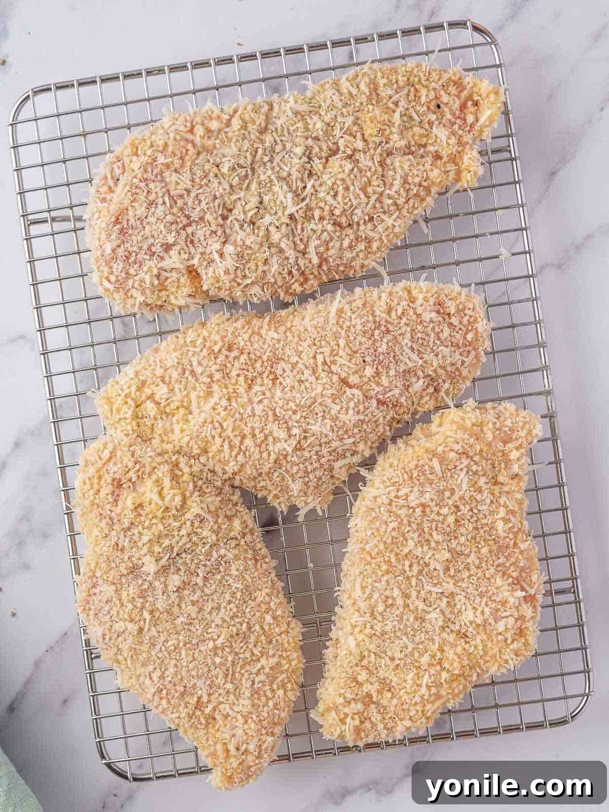 Coated chicken breasts resting on a wire rack before frying.
