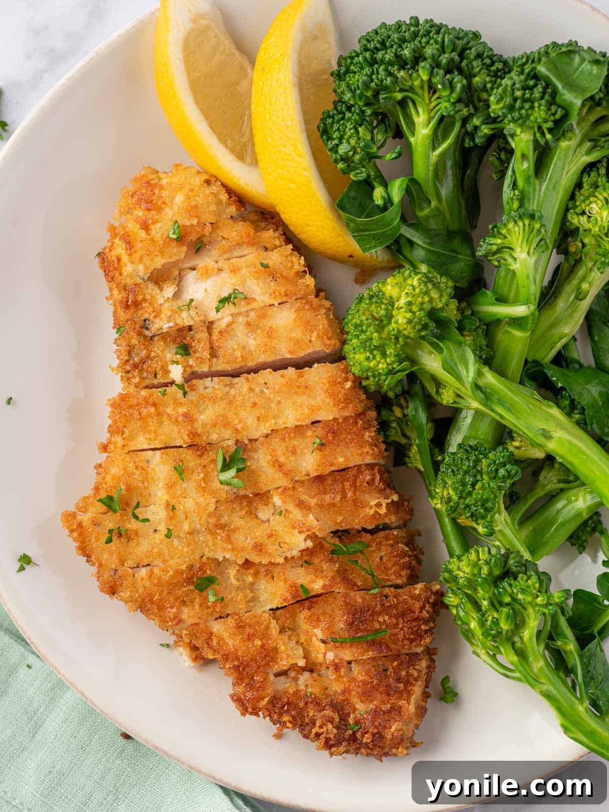 A plate of crispy parmesan chicken breasts served with a side of broccoli.