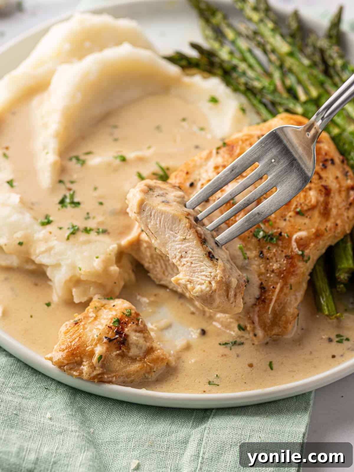 A close-up shot of a piece of creamy garlic parmesan chicken being lifted from a plate, highlighting the tender chicken and the rich, clinging sauce.