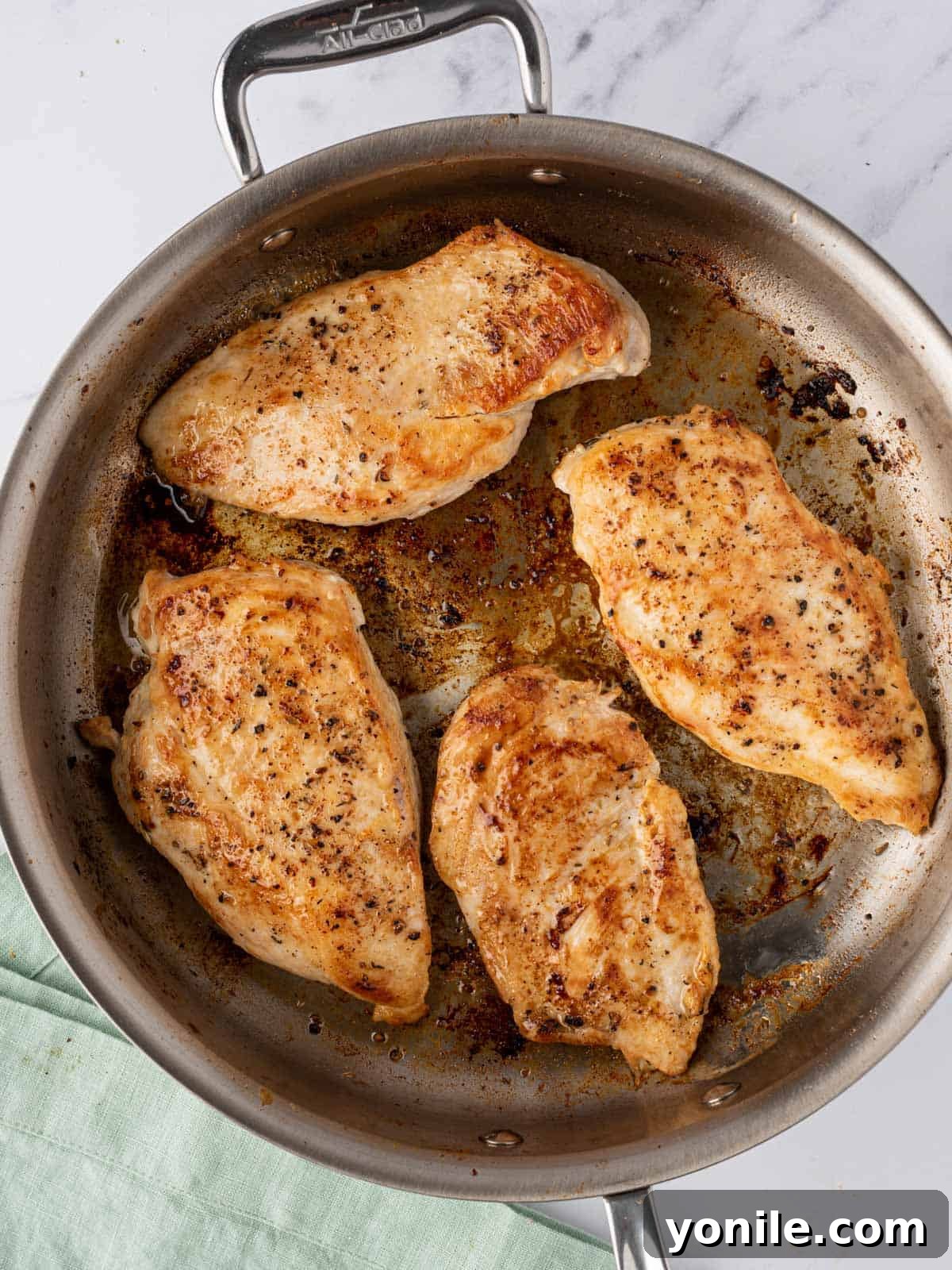 Four golden-brown, seared chicken breasts resting in a pan, cooked to perfection and ready to be set aside for the creamy sauce preparation.