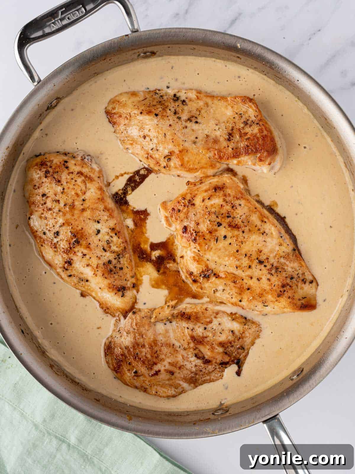 Seared chicken breasts are gently placed back into the skillet, nestled in the creamy garlic parmesan sauce, ready to finish cooking and soak up the flavors.