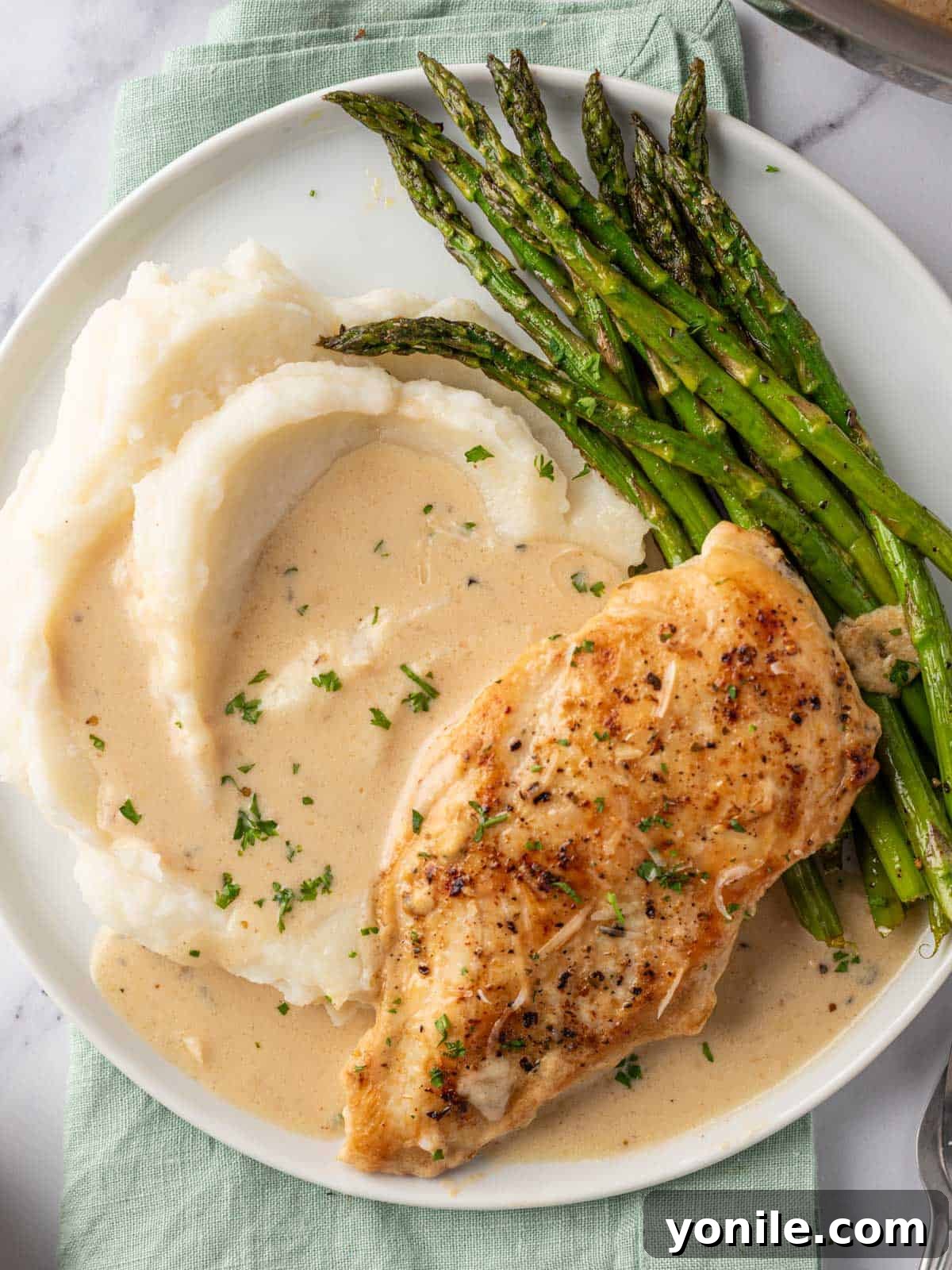 A plated serving of creamy garlic parmesan chicken, accompanied by fluffy mashed potatoes and vibrant green asparagus, ready for a delicious and satisfying meal.