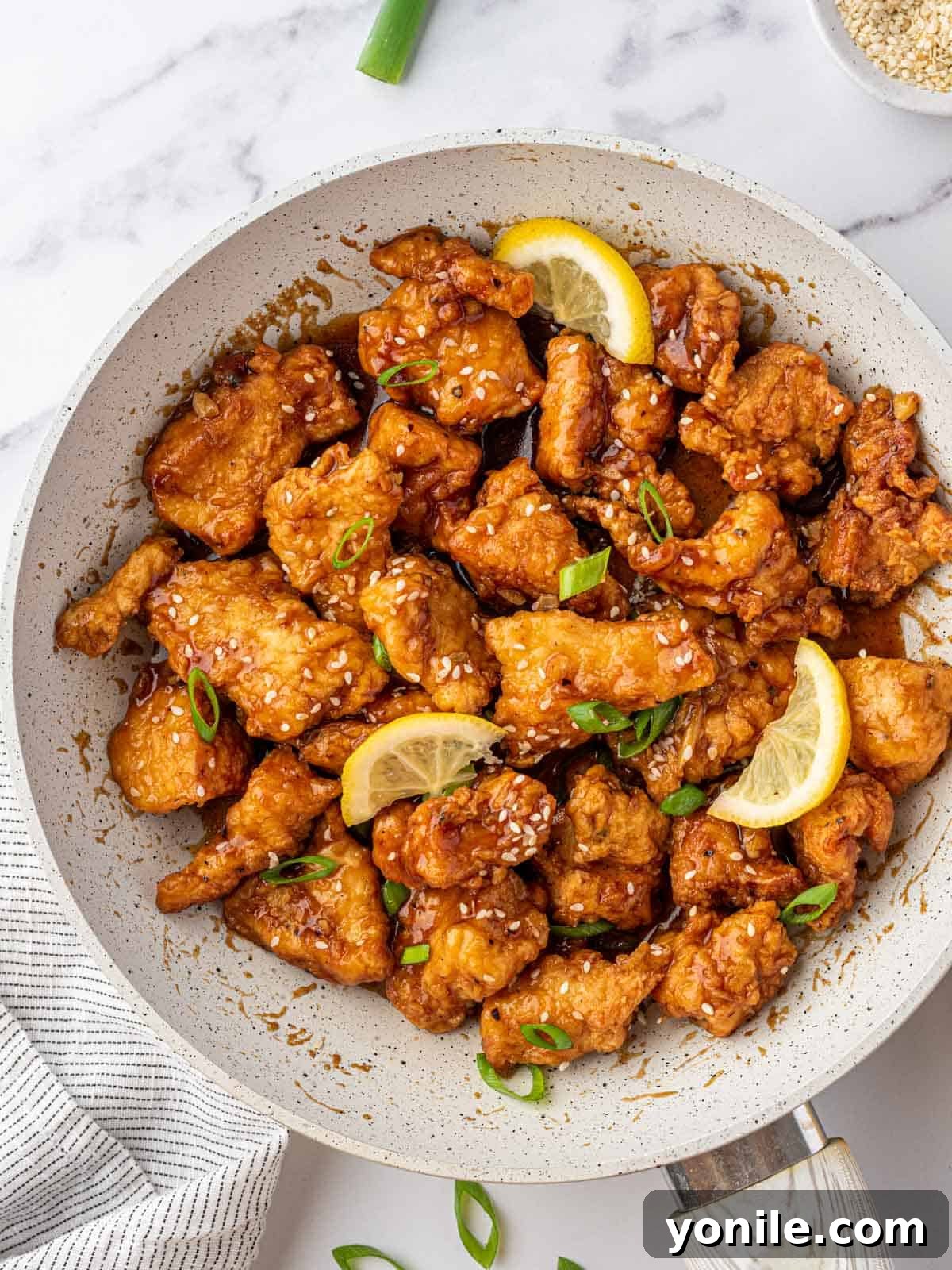 Zesty Lemon Chicken 2 Skillet full of lemon chicken topped with green onions, sesame seeds and three fresh lemon wedges.