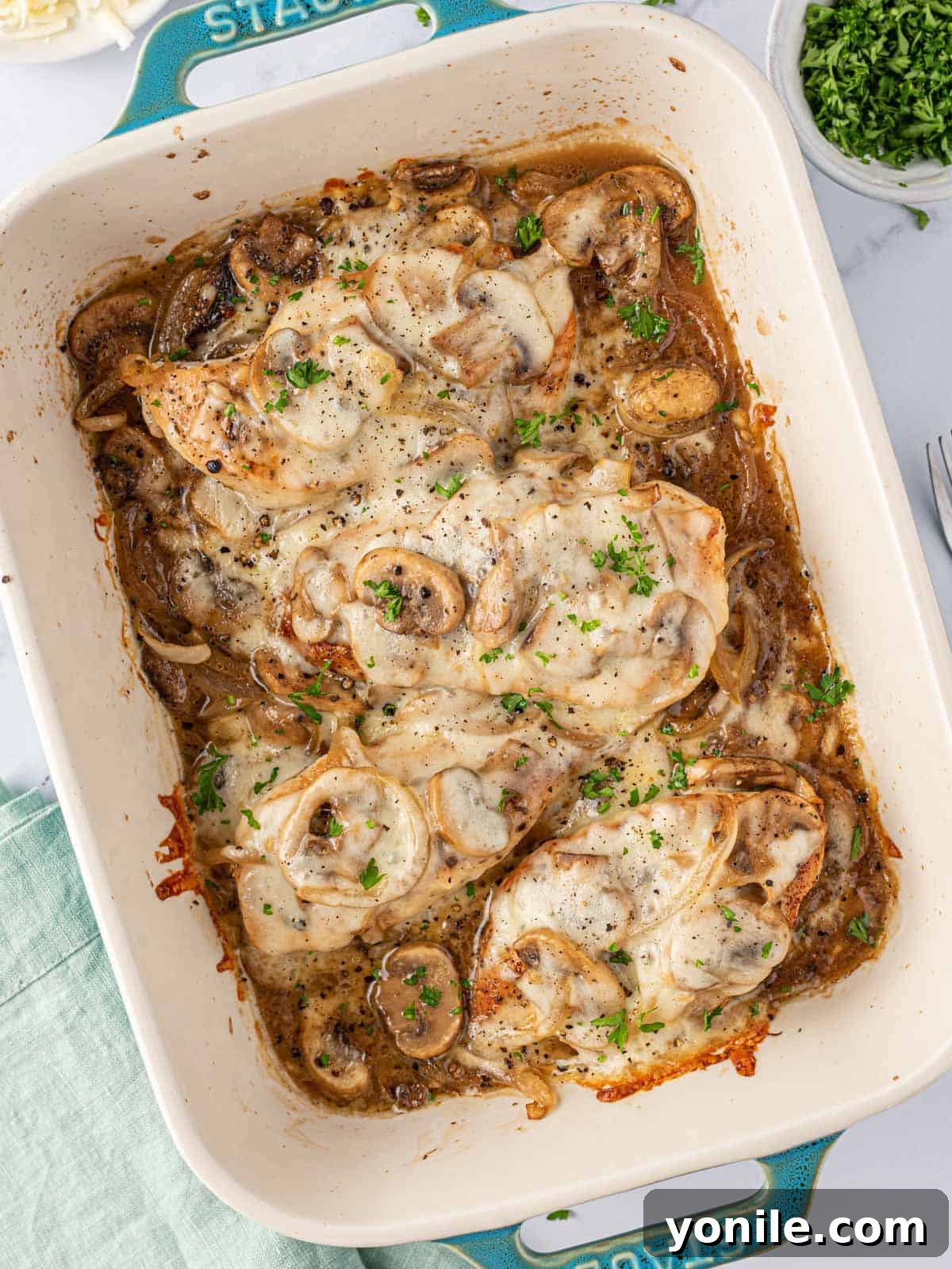 Overhead view of cheesy baked chicken breasts with mushrooms in a blue baking dish, ready to be served.
